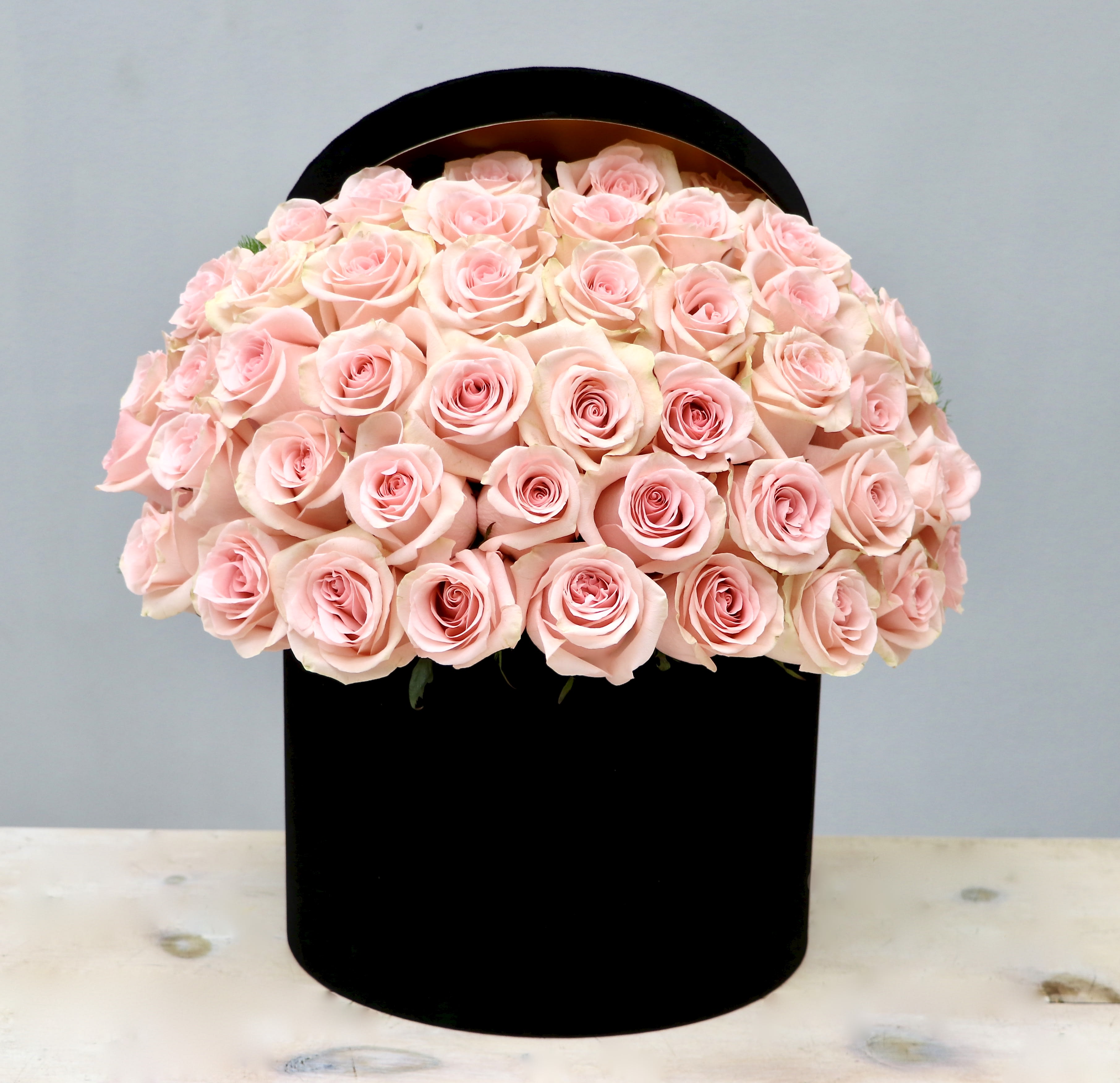 Dome of pale pink roses arranged in a round black hatbox-style container