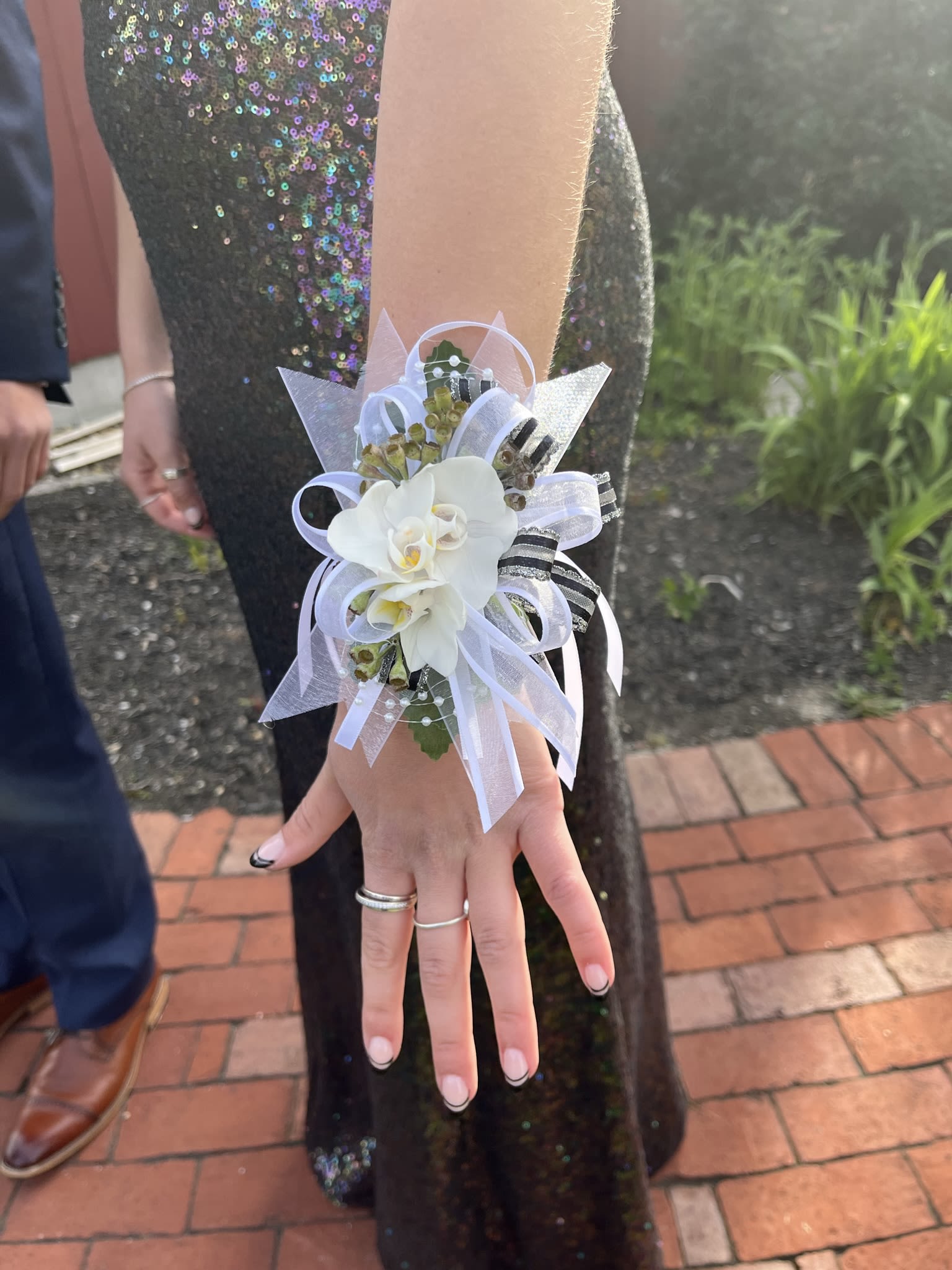 White orchid wrist corsage with white ribbons worn on an arm in a dark sequined dress.