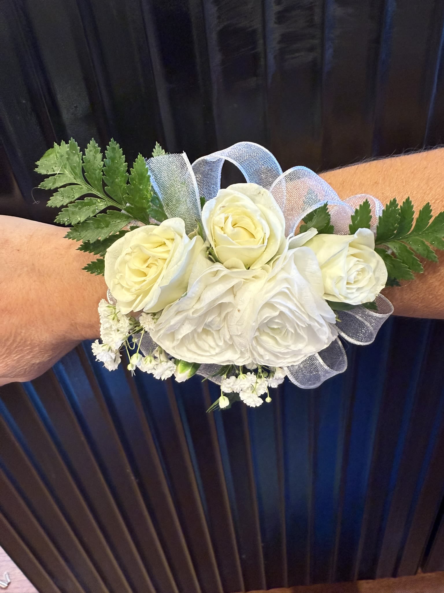 White rose wrist corsage with sheer ribbon accents worn on an arm.