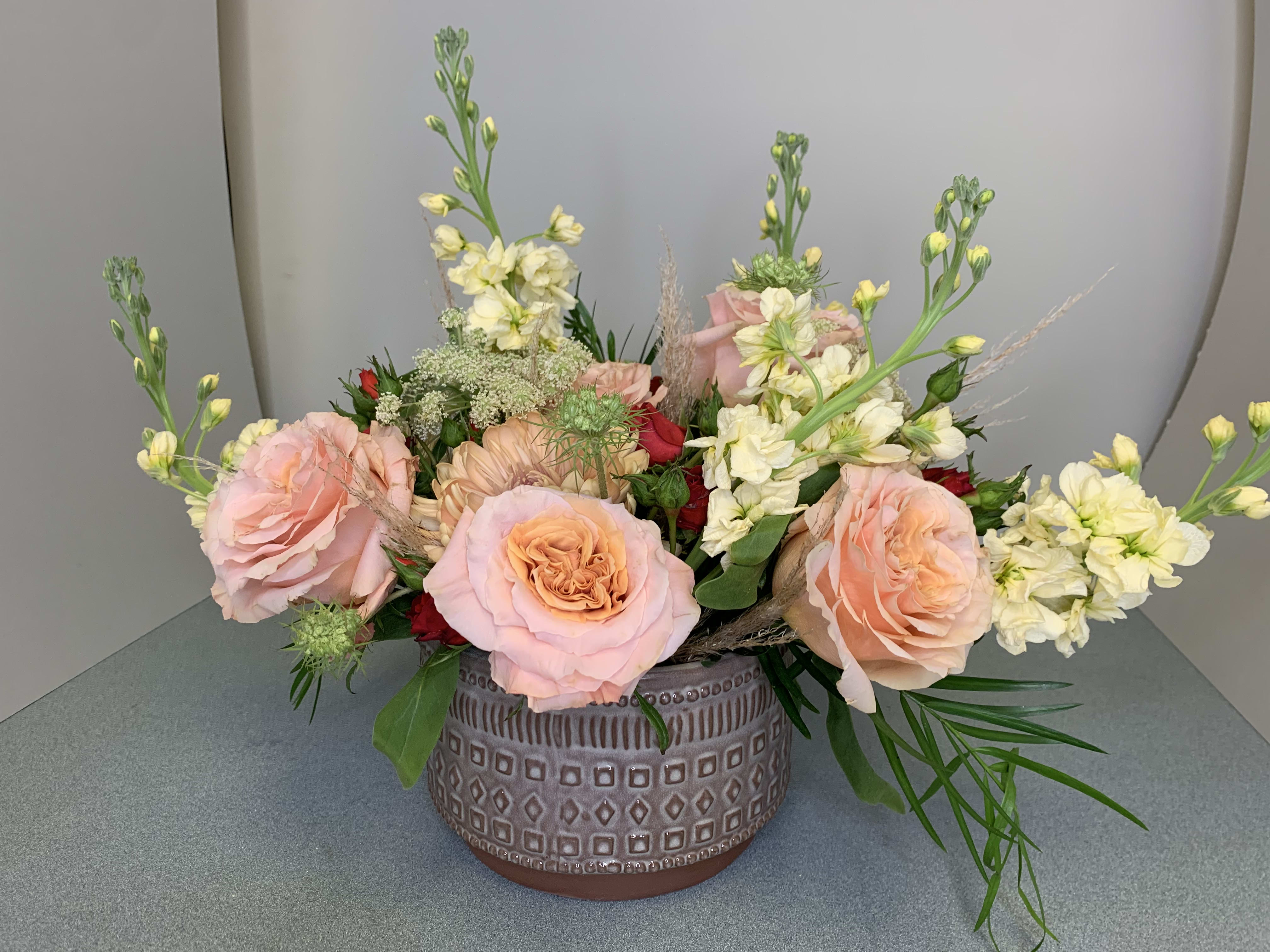 Low floral arrangement of pink roses and cream blooms in a patterned ceramic vase