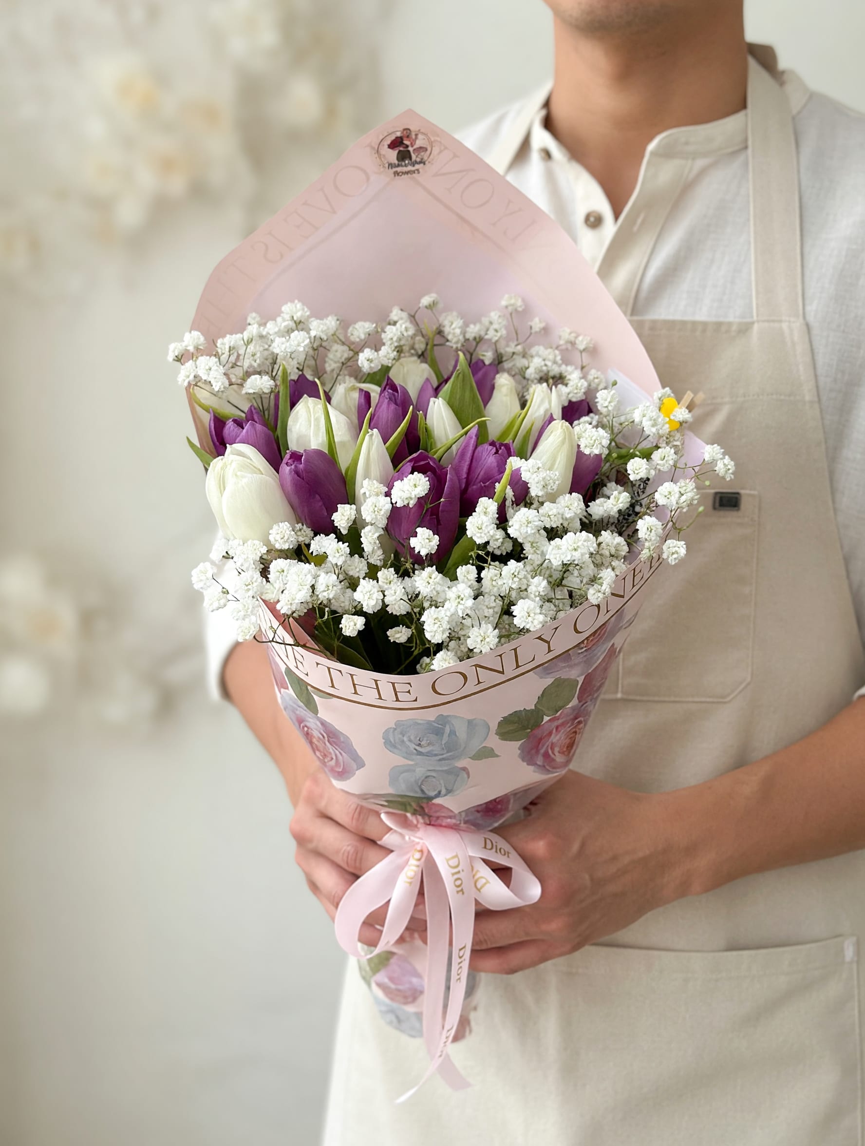 20 Tulips in Fancy Bouquet - A timeless and delicate bouquet featuring a beautiful mix of fresh tulips in soft white and rich purple tones, perfectly complemented by airy baby’s breath for a romantic, cloud-like finish. Wrapped in luxury floral paper and tied with a soft satin ribbon, this arrangement is designed to feel both modern and effortlessly elegant.  Perfect for birthdays, anniversaries, or simply to brighten someone’s day with a refined and graceful touch.   Ideal for: • Birthdays • Romantic gestures • “Just because” moments • Elegant gifting  Please note: Tulip shades may vary slightly based on availability while maintaining the same overall color palette and design style.