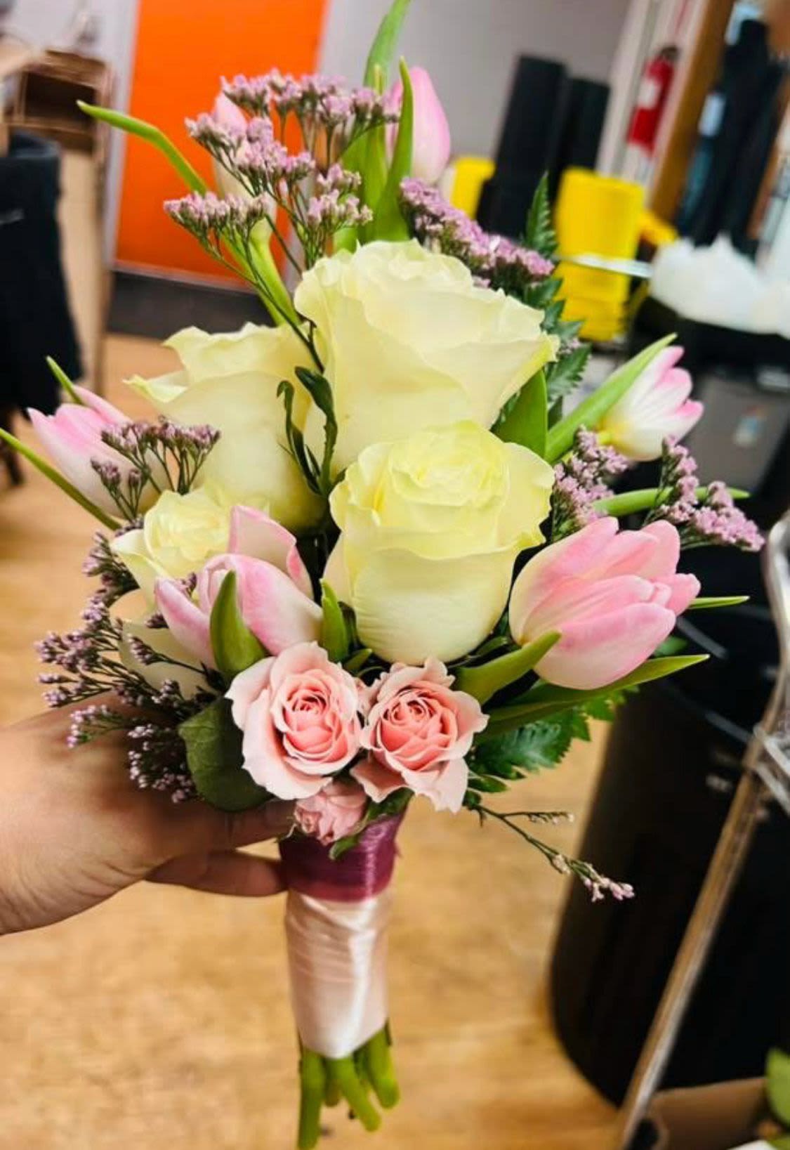 Hand-tied bouquet of cream roses, pink roses, and pink tulips wrapped with pink and ivory ribbon
