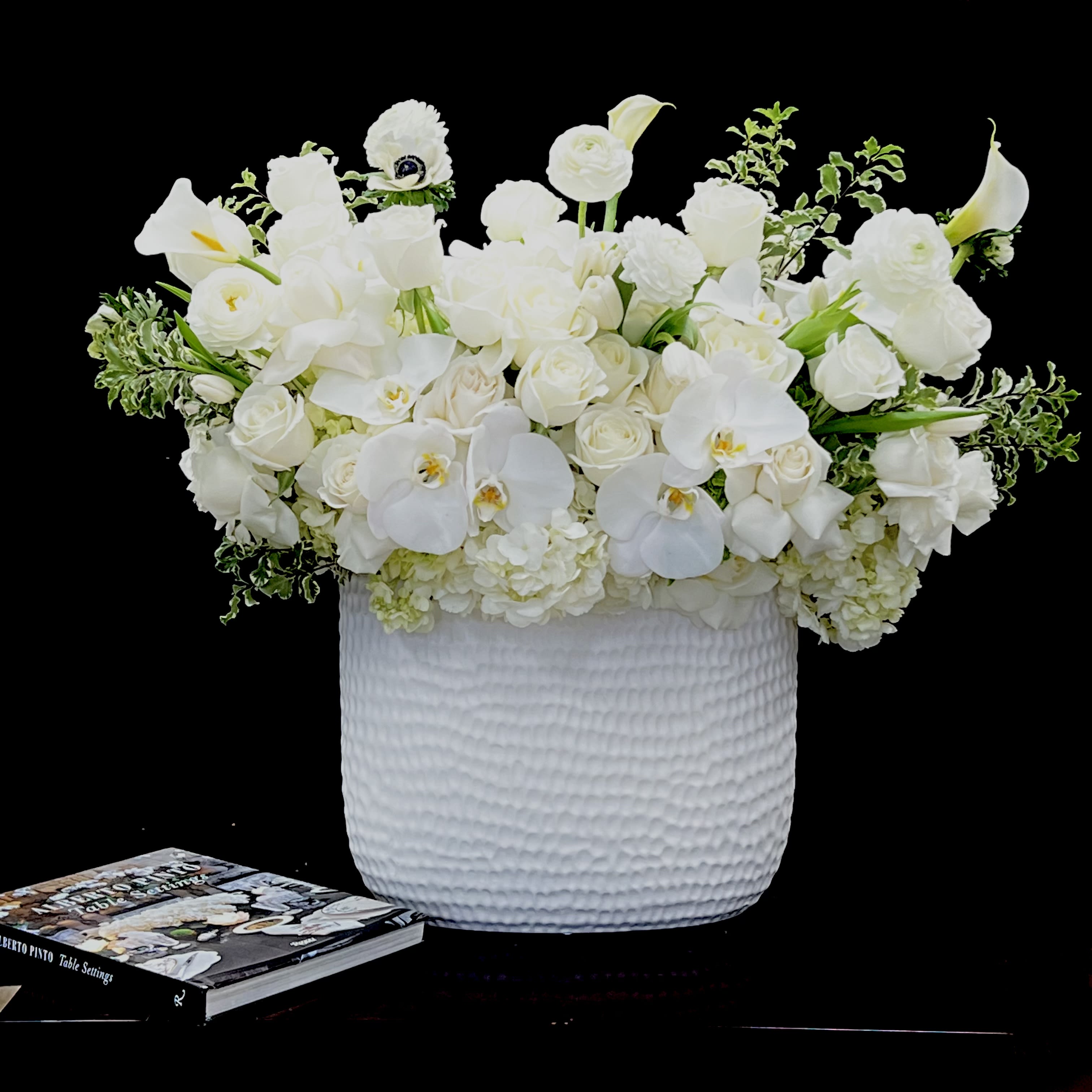 Sweet Unique - This tall vase arrangement features an array of white flowers including Phalaenopsis Orchids, Ranunculus, Calla Lilies, Roses, Tulips, and Hydrangea
