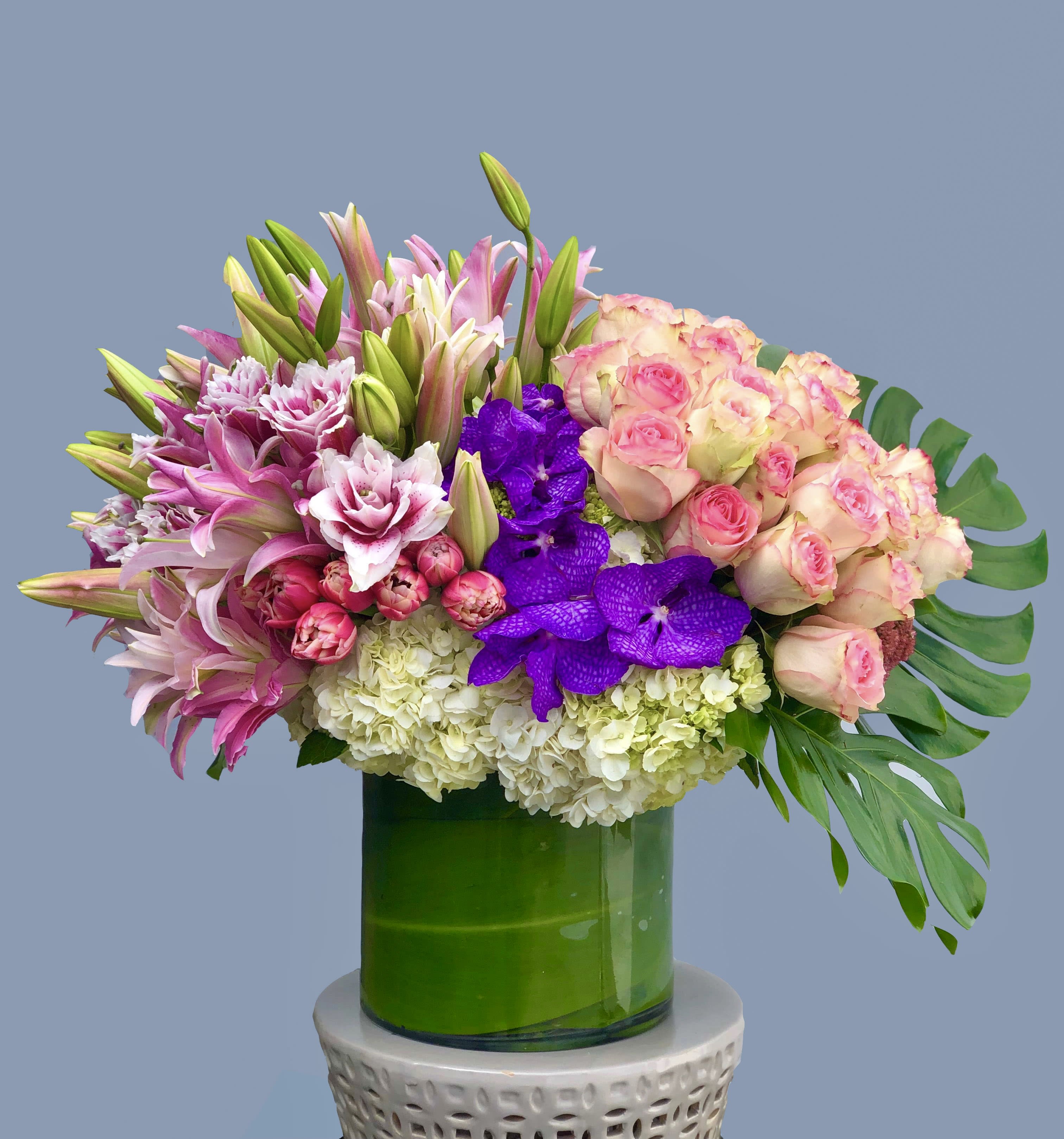Enchanted Flowers - A combination of pink Roses, Tulips, and Lilies, with purple Vanda Orchids and white Hydrangea, in a leaf-lined glass vase