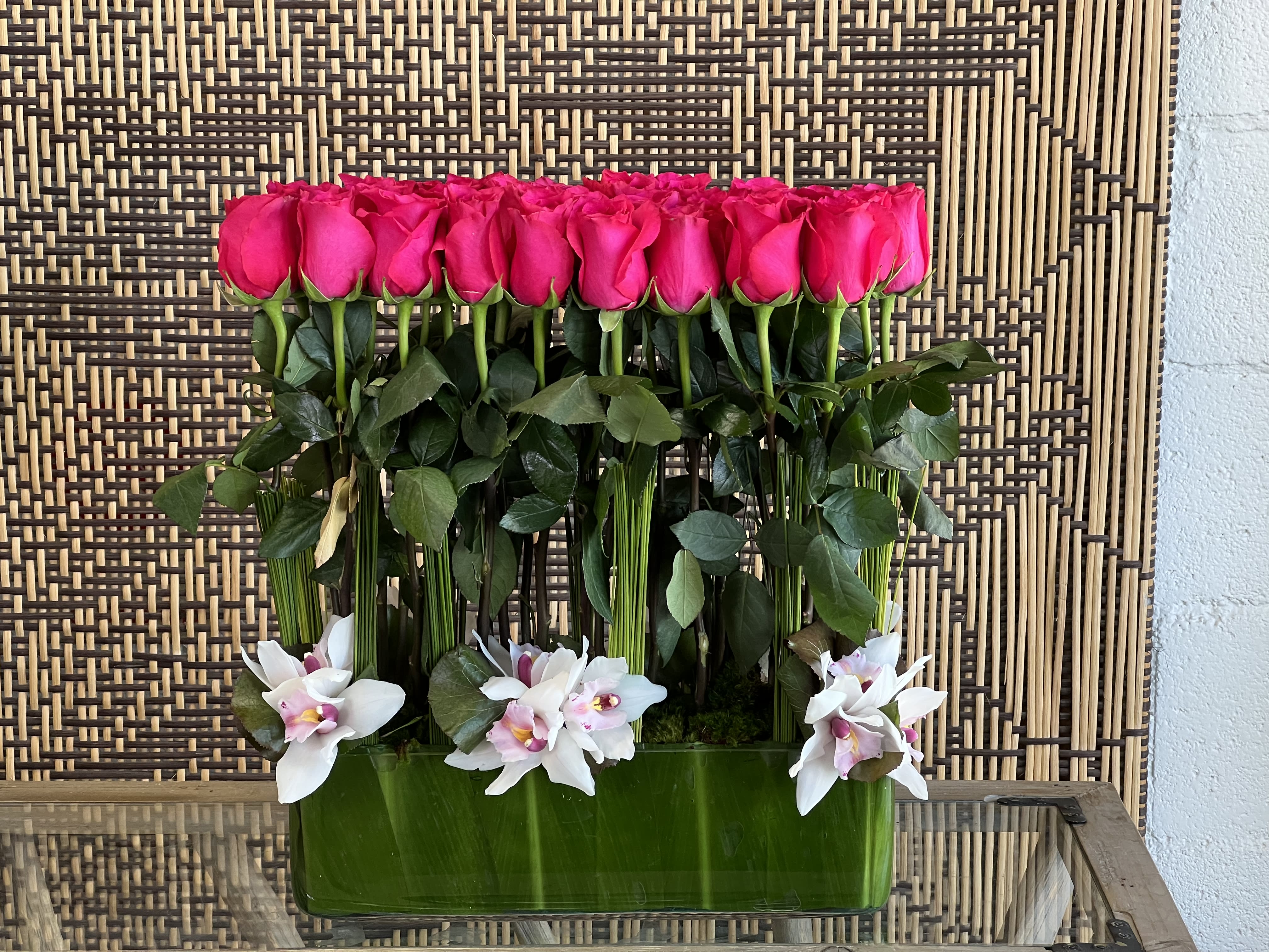 Hot Touch - A modern arrangement of Roses and Cymbidium Orchids, presented in a leaf-lined vase