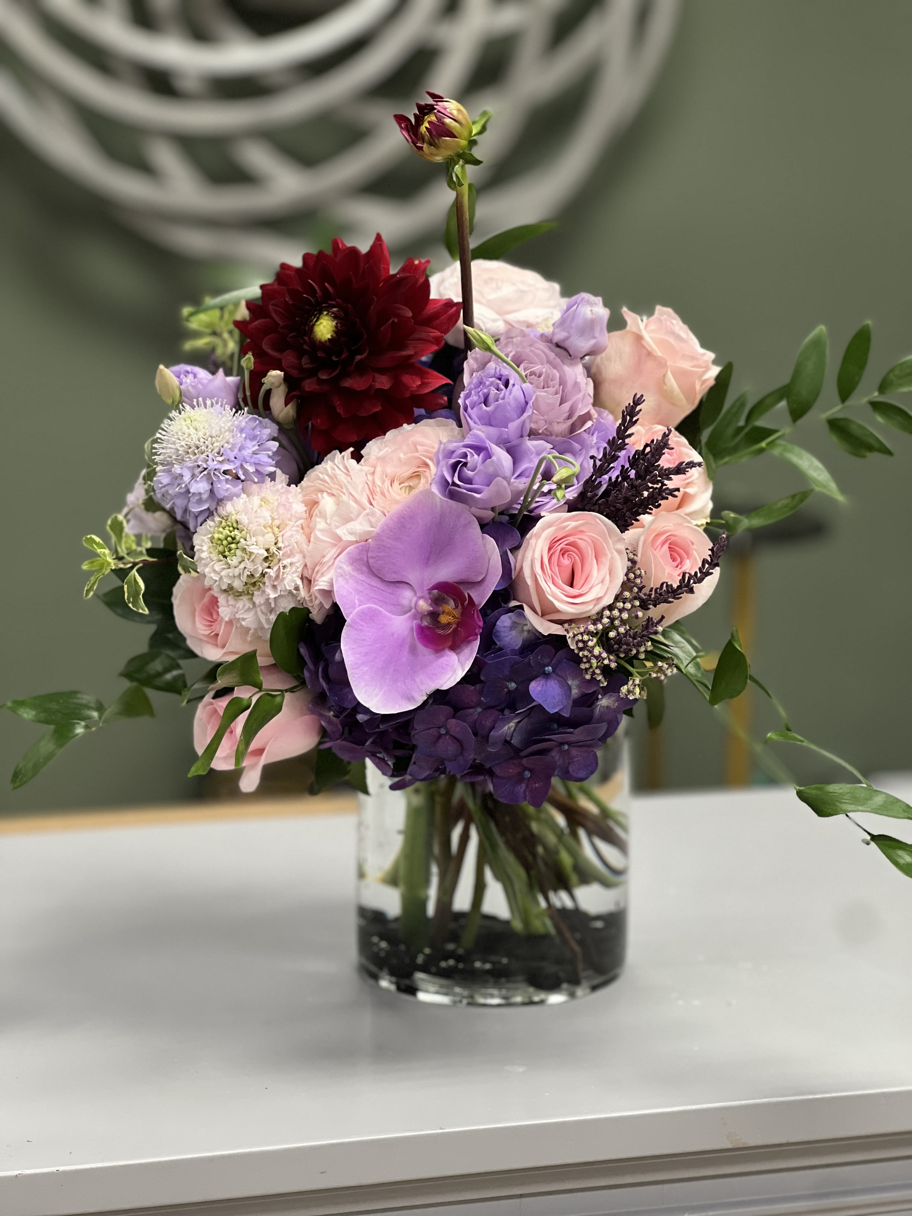 Mixed pink, purple, and burgundy flowers arranged in a clear glass vase