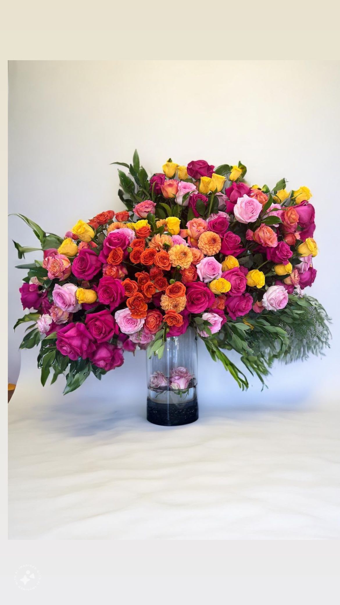 Jacklyn  - A large mix of colorful flowers, including Roses and Dahlias, set atop a tall glass cylinder vase