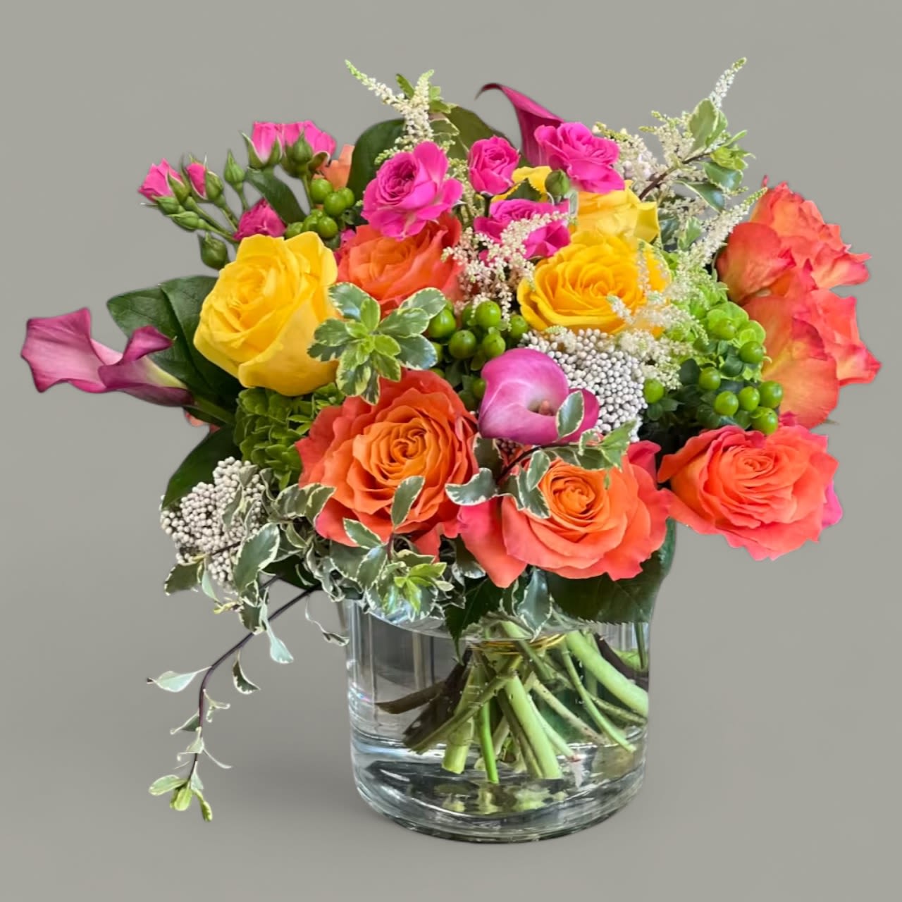 Dominic - This petite, colorful floral arrangement is a great way to bring a pop of color to the office or home! Roses, Spray Roses, Hydrangea, and Calla Lilies with greenery and other filler flowers, arranged in a cylindrical glass vase