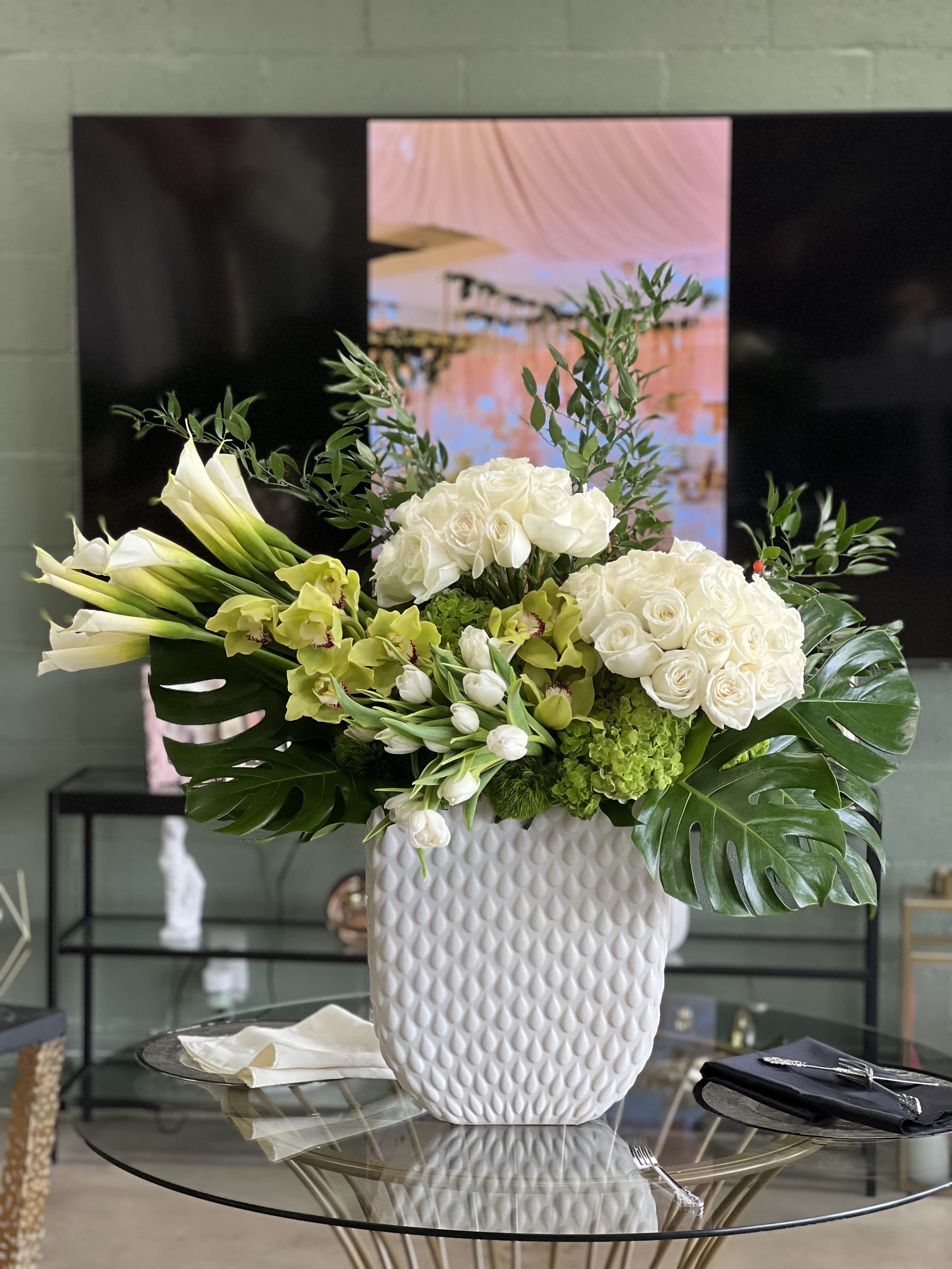 Belinda - This luxurious modern arrangement features clusters of white Roses, set against dramatic bursts of Calla Lilies, Tulips, and Cymbidium Orchids. Finished with Monstera leaves and elegant Italian Ruscus