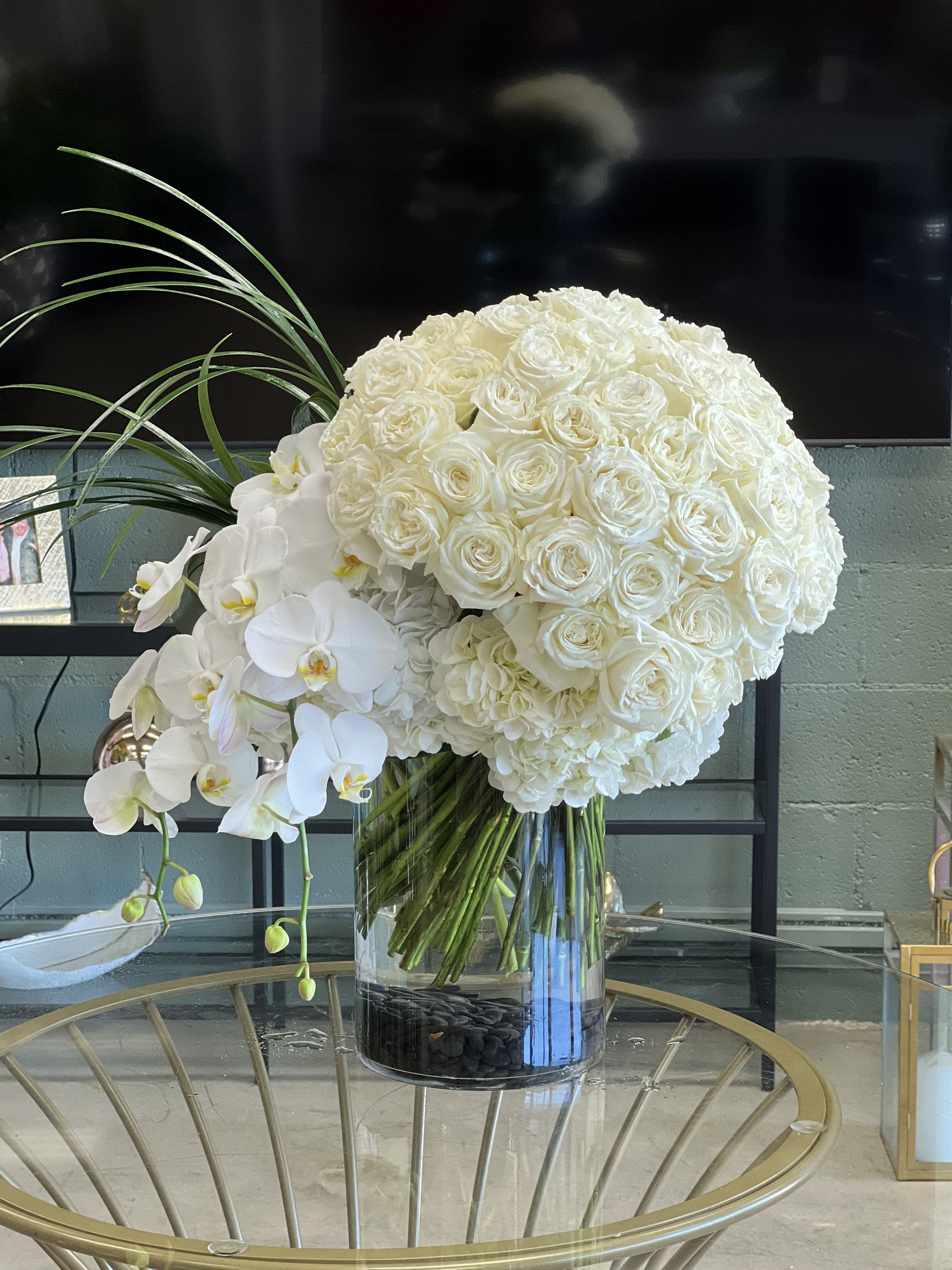 Polar  - This stylish, modern floral arrangement features a tight cluster of white Roses, set in a bed of Hydrangea, with a cascade of Phalaenopsis Orchids and a plume of grass