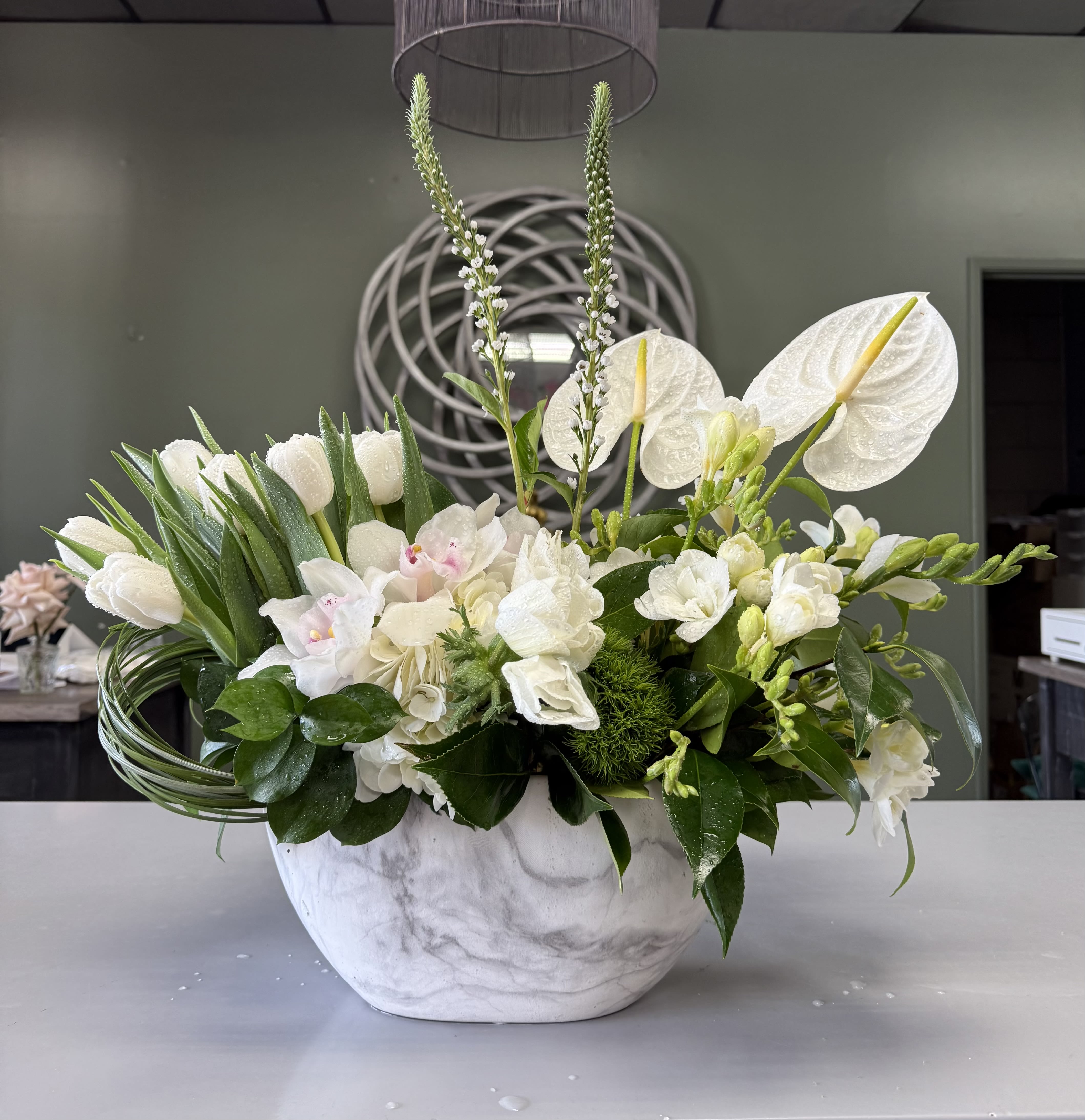 Headlock - An architectural twist of mixed white flowers, composed of Tulips, Anthurium, Cymbidium Orchids, Trick Dianthus, Freesia, and Bear Grass