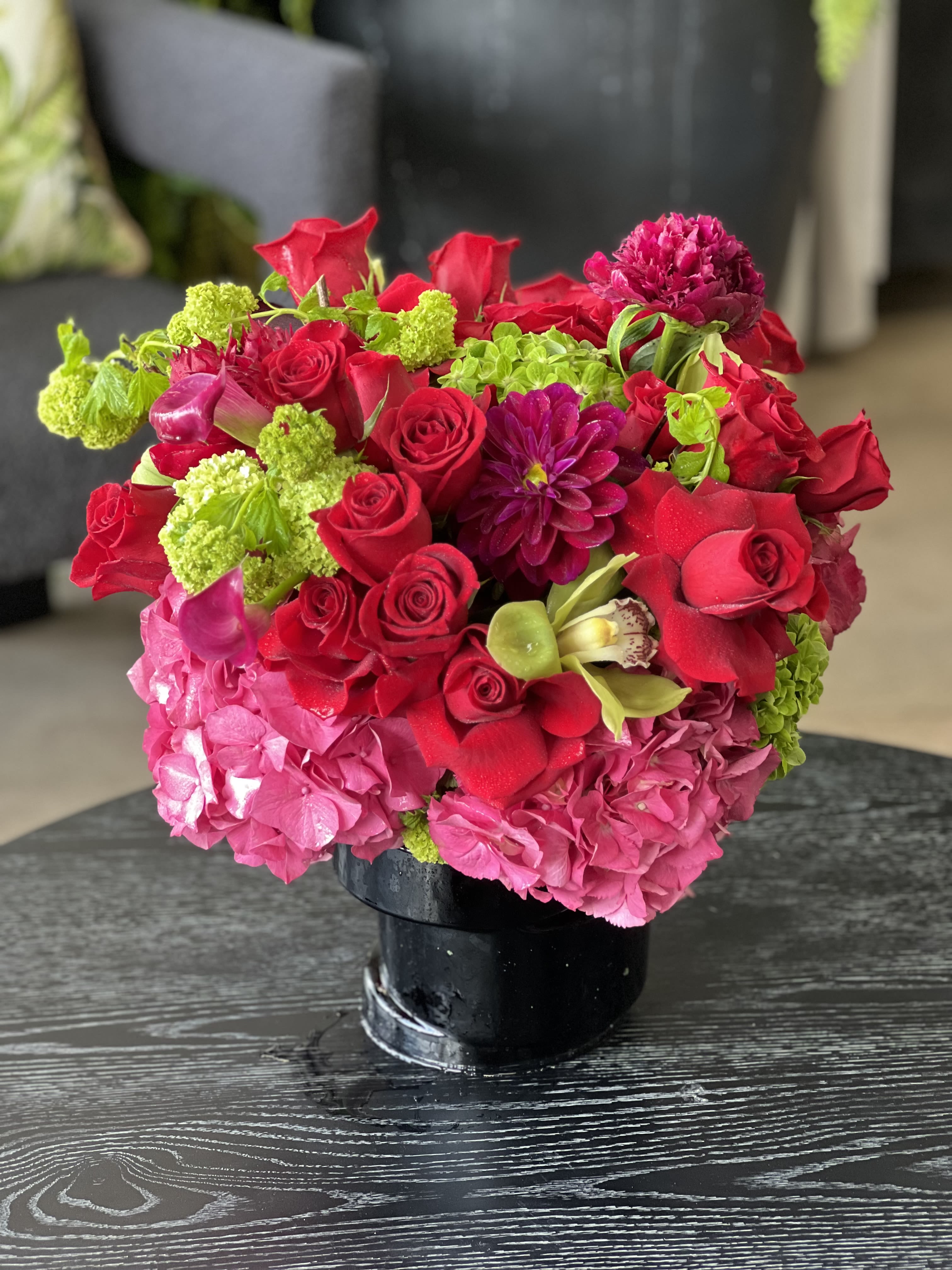 Raspberry  - This bright and colorful arrangement features Hydrangea, Roses, Dahlias, and Cymbidium Orchids in a ceramic vase