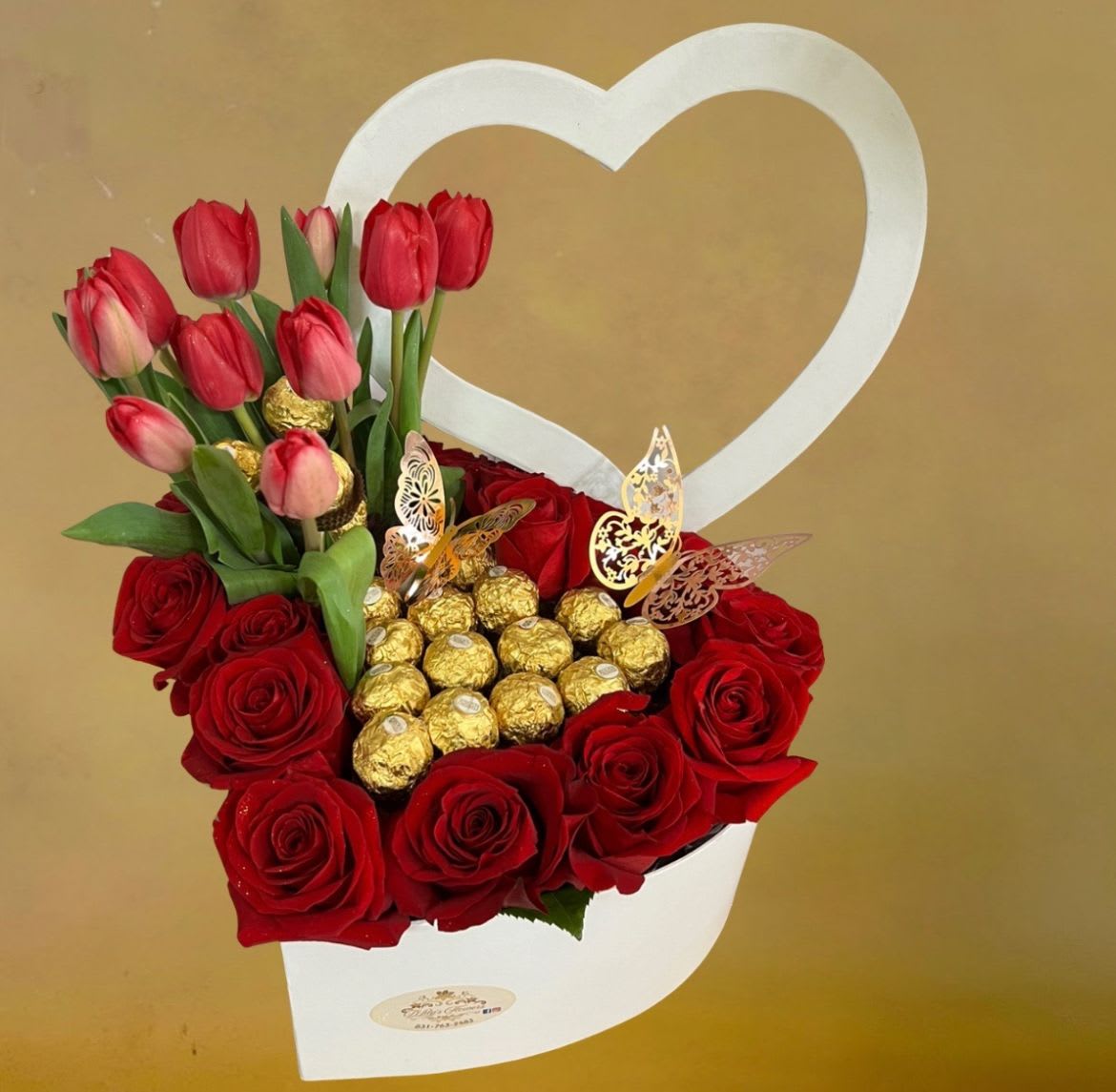 Heart-shaped white box with red roses, red tulips, and gold-wrapped chocolates.