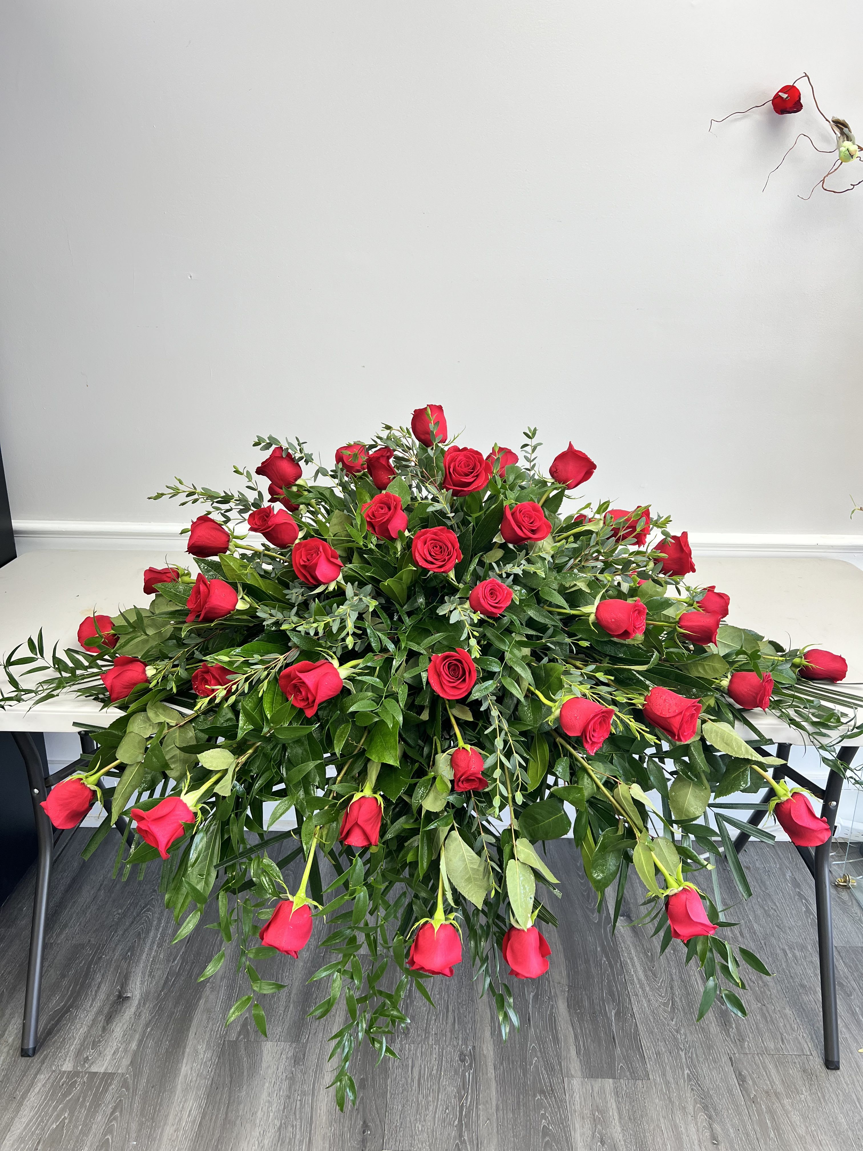 Red Rose Half Casket Spray - An abundance of red roses will express your love and devotion with beauty. This classic casket spray of roses mixed with greenery will be a fragrant reminder on a solemn day.