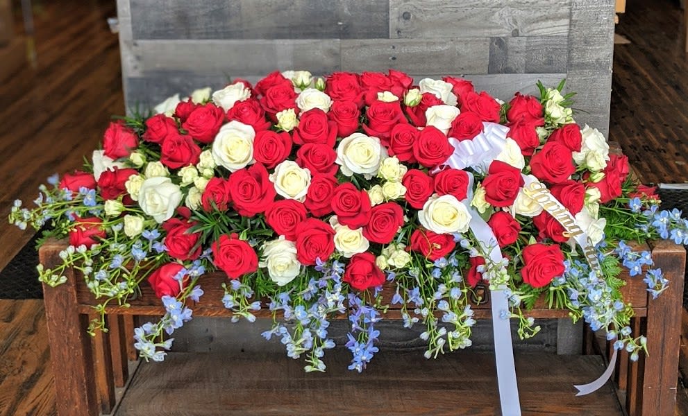 Large red and white rose casket spray with trailing light blue flowers and white ribbon