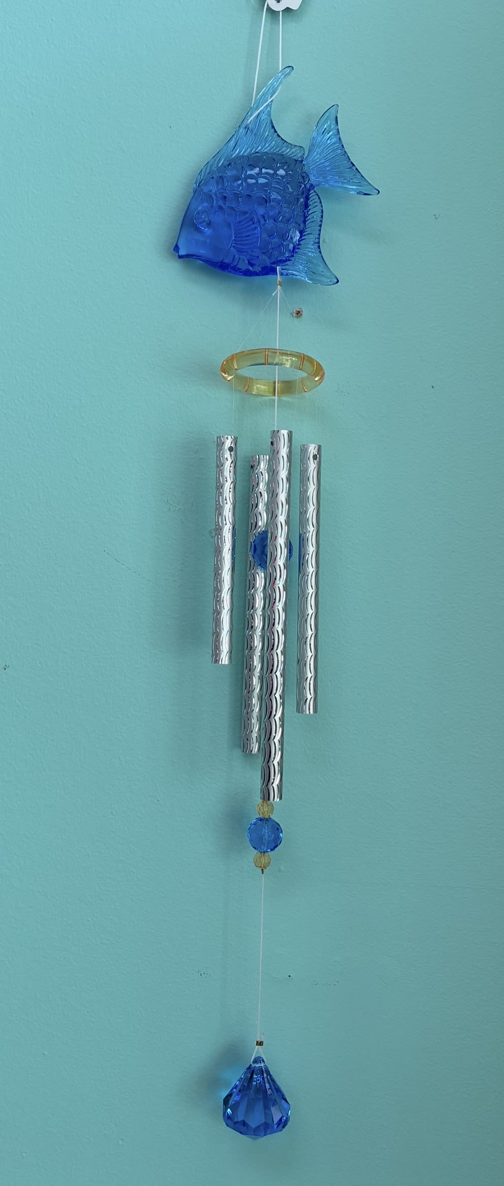 Hanging wind chime with blue fish, silver tubes, and blue crystal drop on a teal wall