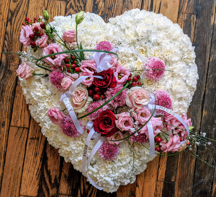 Heart-shaped white floral tribute with pink and red flowers and white name ribbons