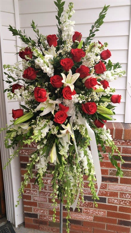 Tall standing spray of red roses, white lilies, and white flowers on a metal easel