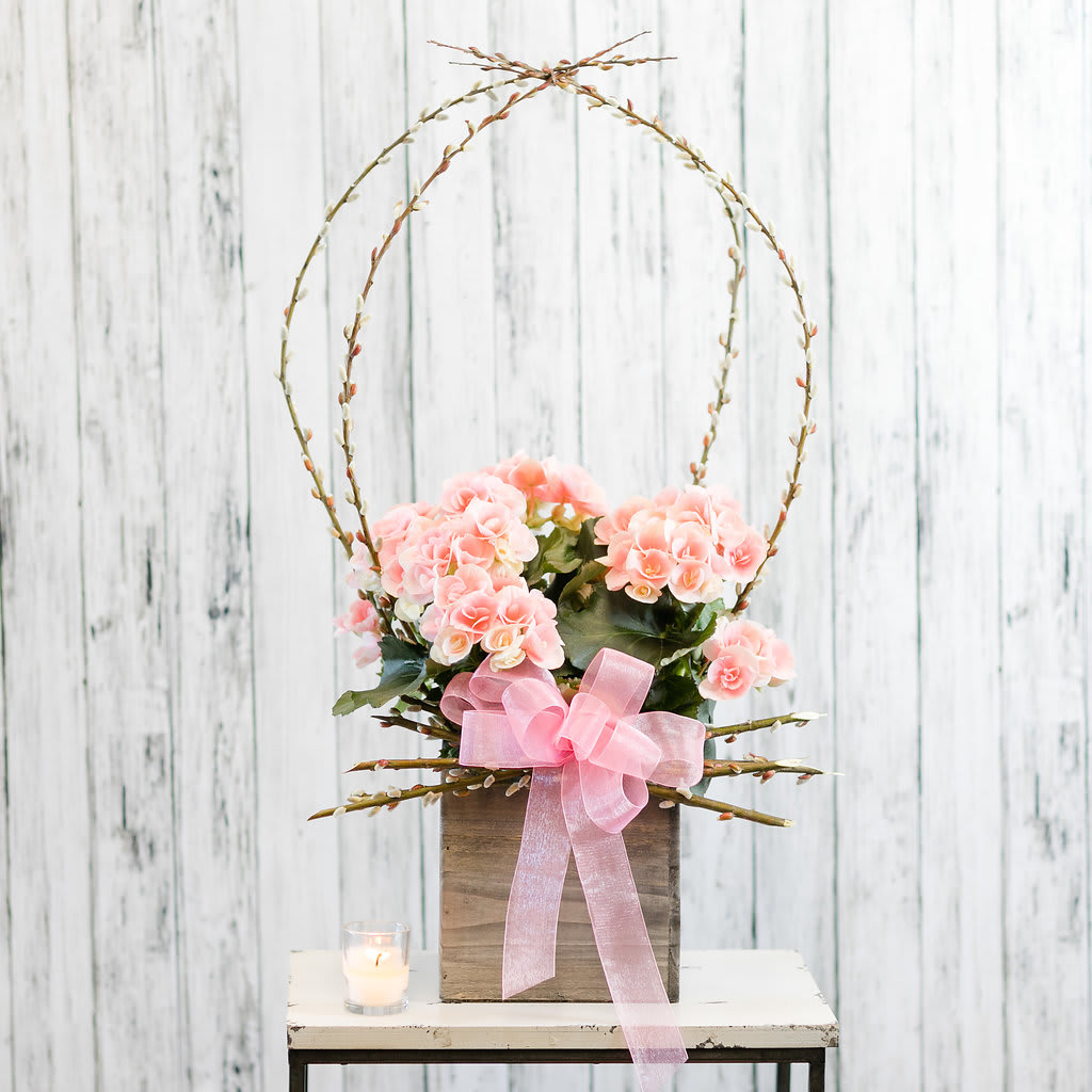 Pink flower arrangement in a rustic wooden box with tall twig arches and a sheer pink bow.
