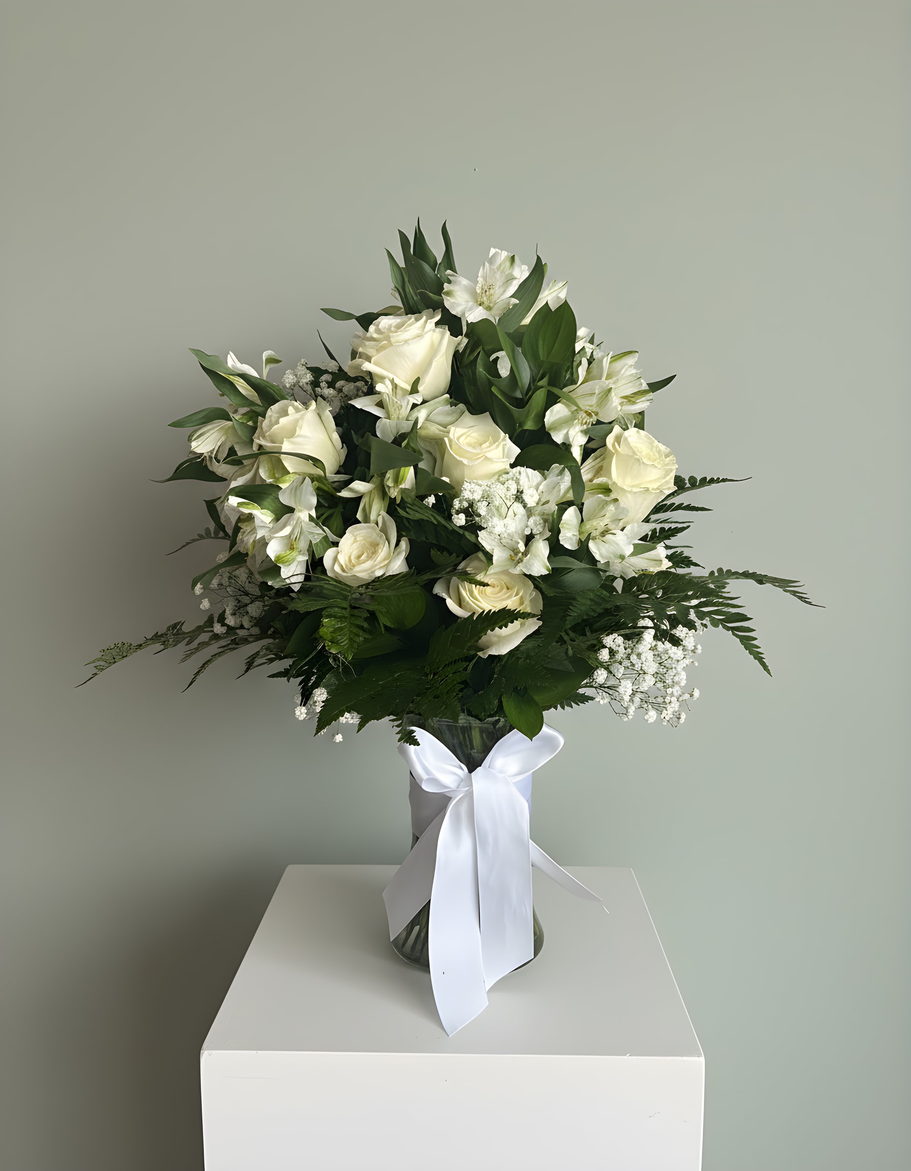 12 Rose &amp; Astromelia Vase Arrangement - A timeless and sophisticated arrangement featuring a graceful blend of premium white blooms and lush greenery. Designed with classic white roses, delicate lilies and seasonal florals, this piece offers a clean, serene, and elegant presentation.  Arranged in a clear glass vase and finished with a soft white ribbon, this design is perfect for expressing sympathy, celebrating life’s meaningful moments, or adding a touch of refined beauty to any space.   Ideal for: • Sympathy &amp; condolences • Get well wishes • Elegant home décor • Special occasions  Please note: Flower varieties may vary based on availability, while maintaining the same color palette, style, and fullness of the arrangement.