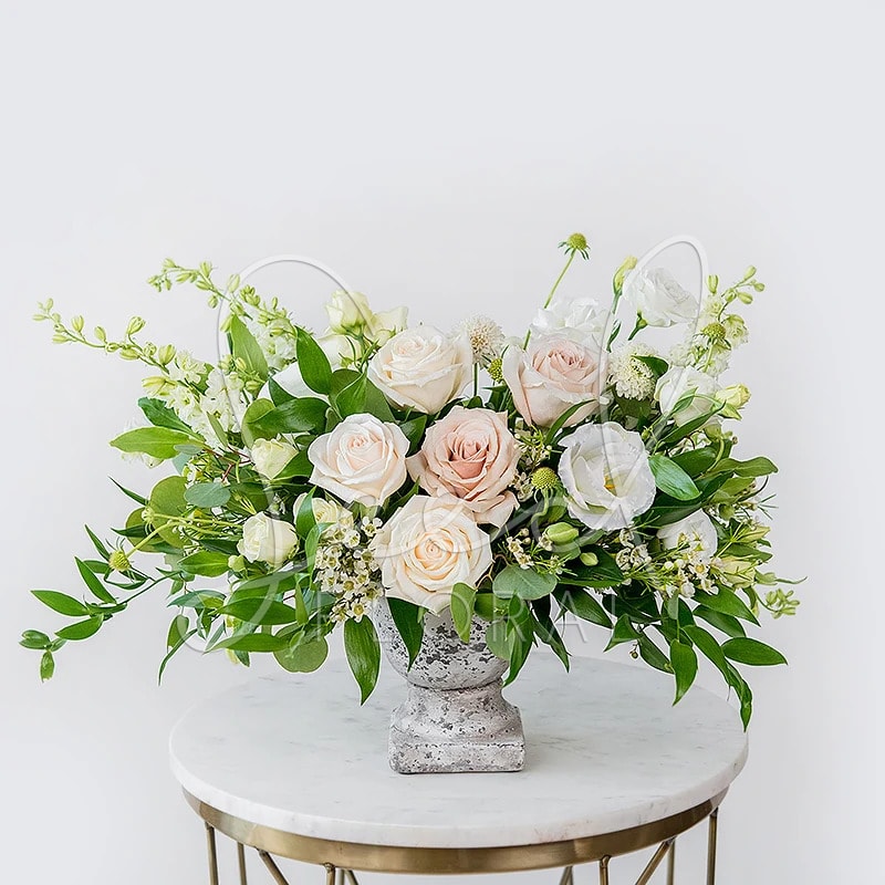 Blush and white roses arranged in a gray pedestal vase