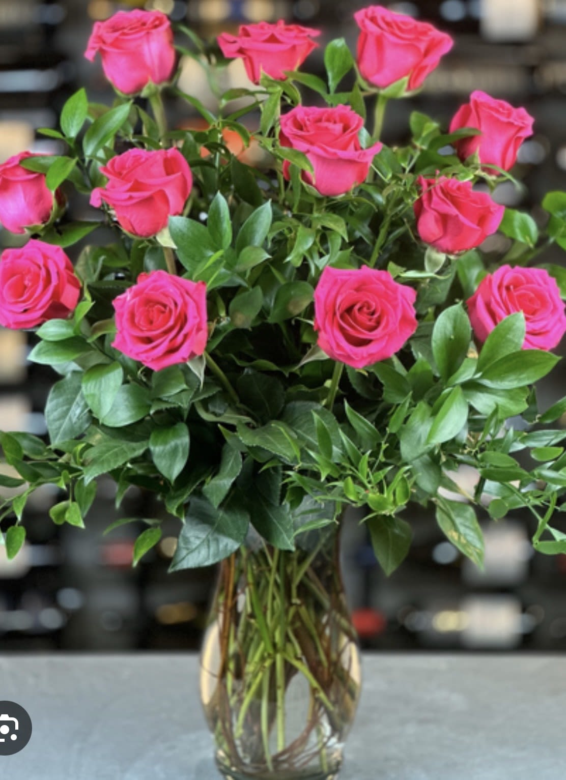 Tall arrangement of bright pink roses with lush greenery in a clear glass vase