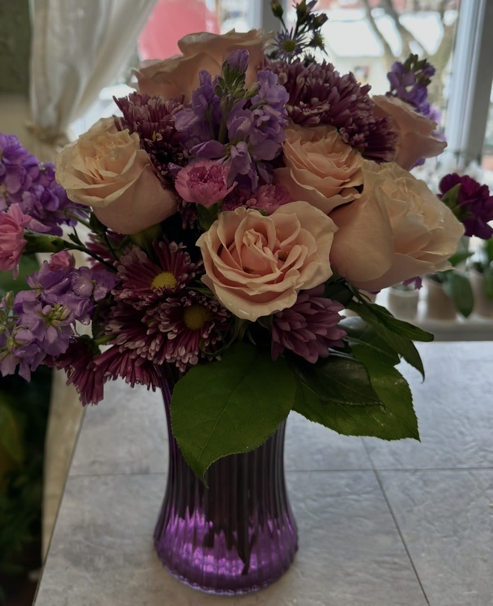 Peach roses with purple and pink blooms arranged in a ribbed purple glass vase