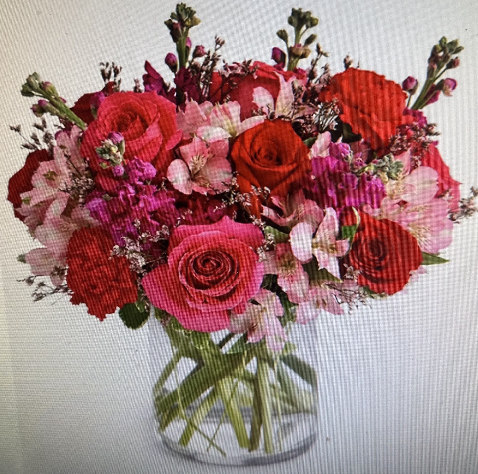 Round arrangement of red and pink roses, carnations, and alstroemeria in a clear glass vase