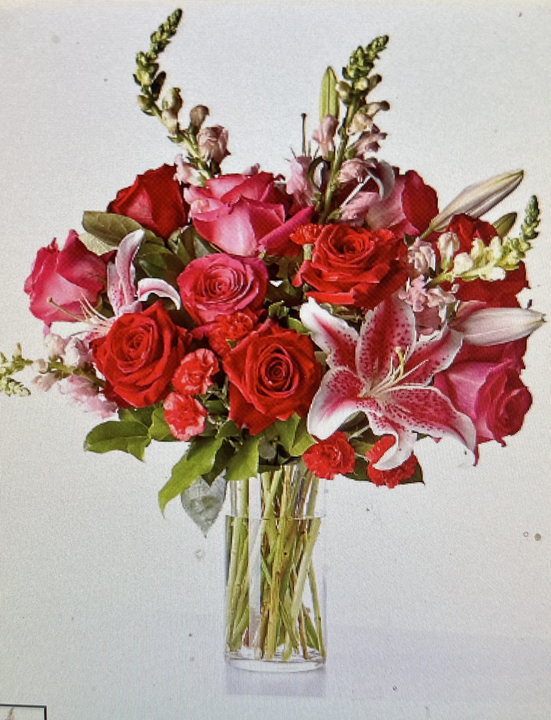 Tall arrangement of red and pink roses, lilies, carnations, and snapdragons in a clear glass vase.