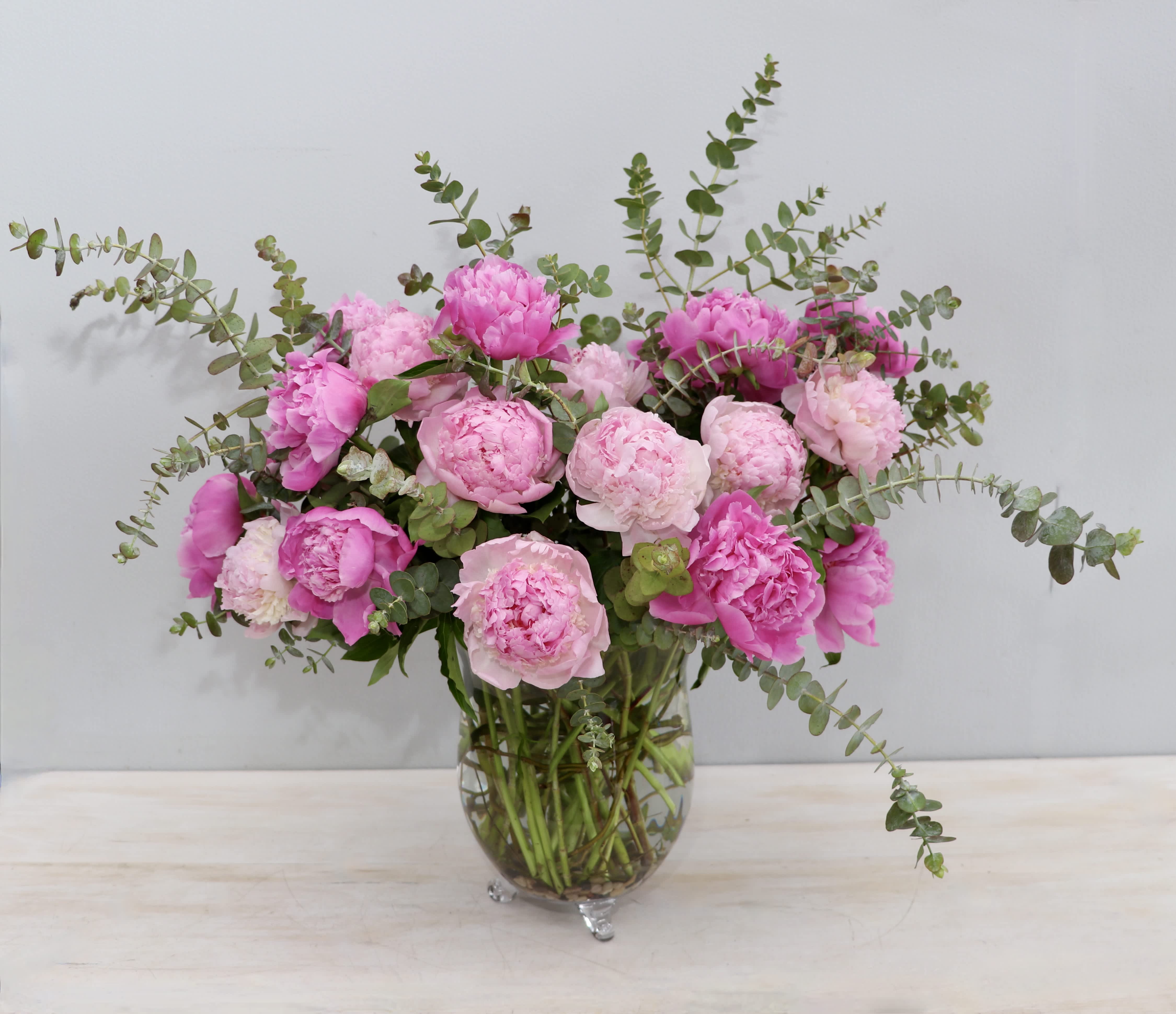 Large arrangement of pink peonies with arching eucalyptus in a clear glass vase