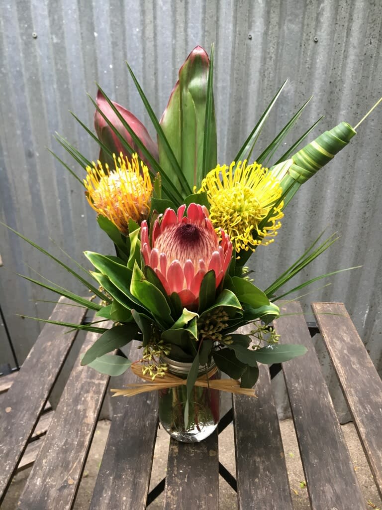Tropical-style bouquet with pink and yellow protea in a clear glass jar vase
