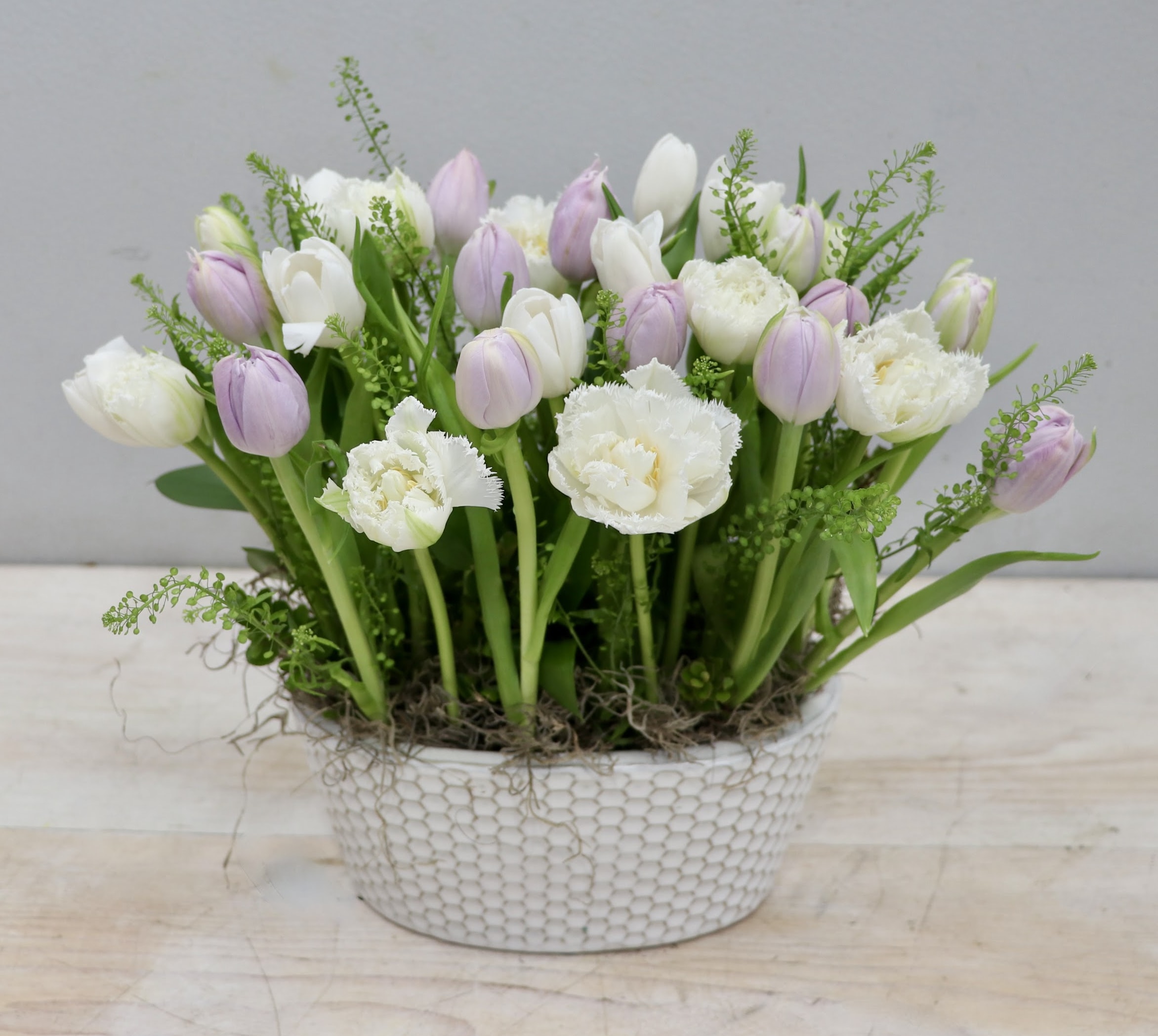 Low arrangement of white and pale lavender tulips in a textured white ceramic bowl