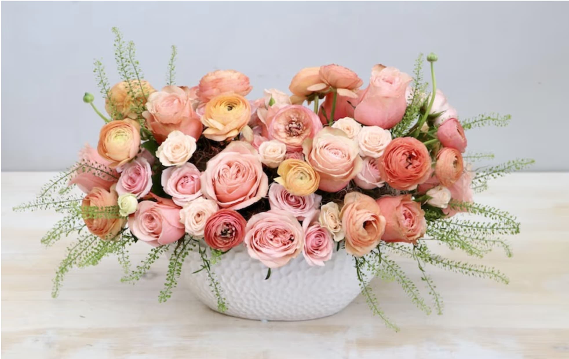 Low arrangement of peach and pink roses and ranunculus in a white ceramic bowl