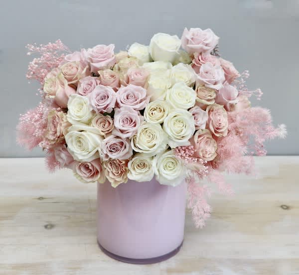 Round arrangement of pale pink and cream roses in a glossy light pink cylinder vase