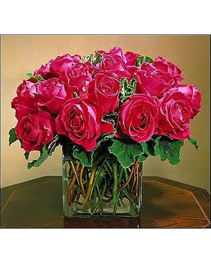 Compact arrangement of hot pink roses in a clear glass cube vase on a wooden table