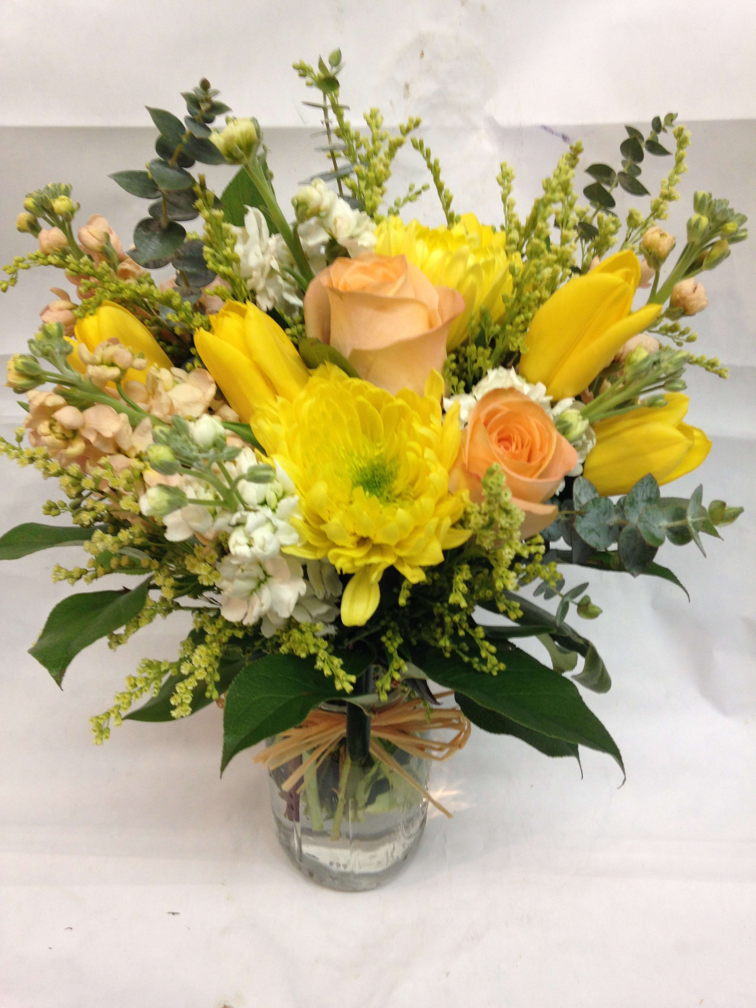 Yellow and peach flower arrangement with roses and tulips in a clear glass jar tied with raffia