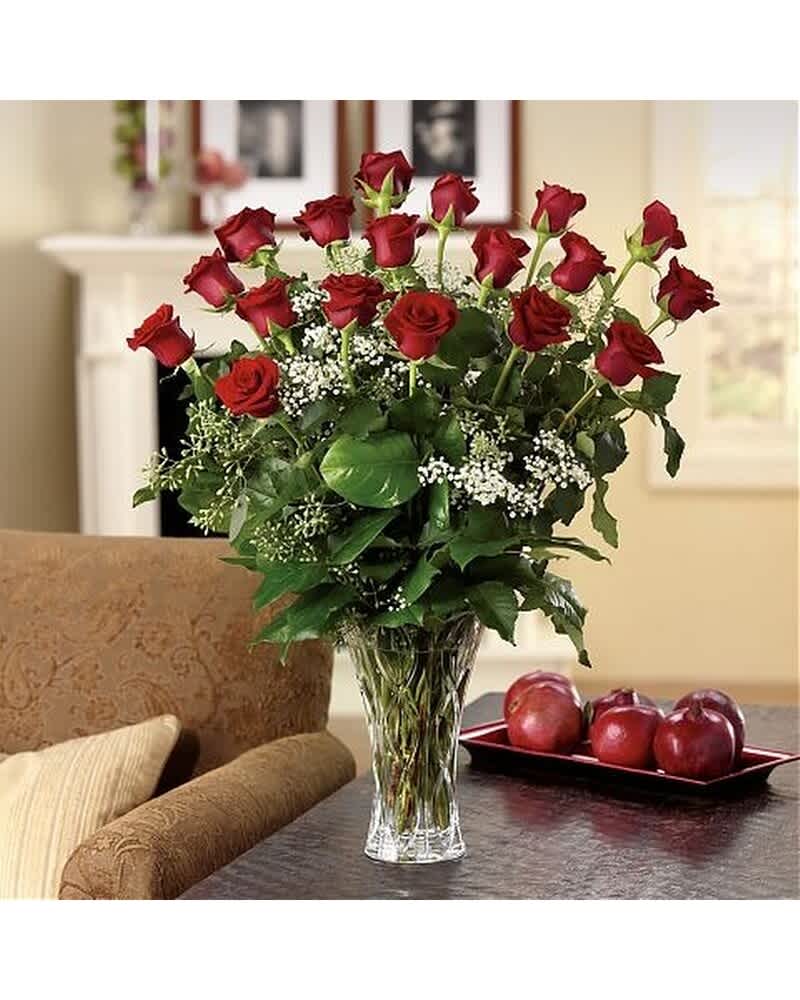 Tall arrangement of long-stem red roses with small white filler flowers in a clear glass vase
