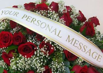 Spray of red roses and white filler flowers with a personalized message banner across the front