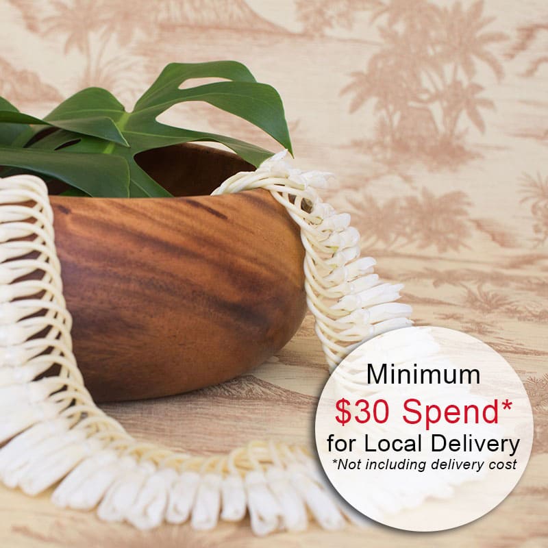 Wooden bowl with a green tropical leaf and white shell lei draped over the rim.