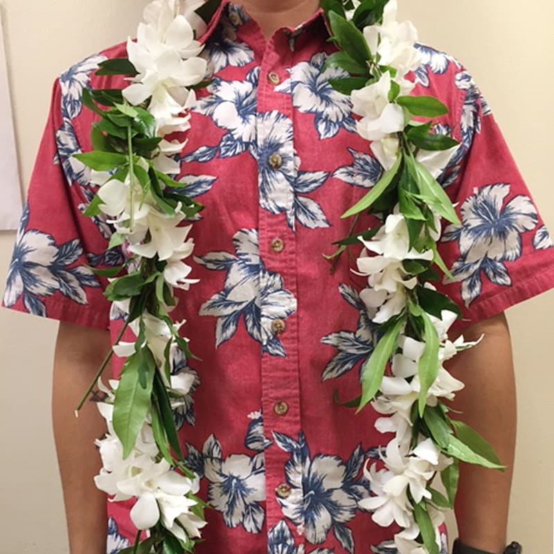 White floral leis with green accents draped around a neck over a red floral shirt