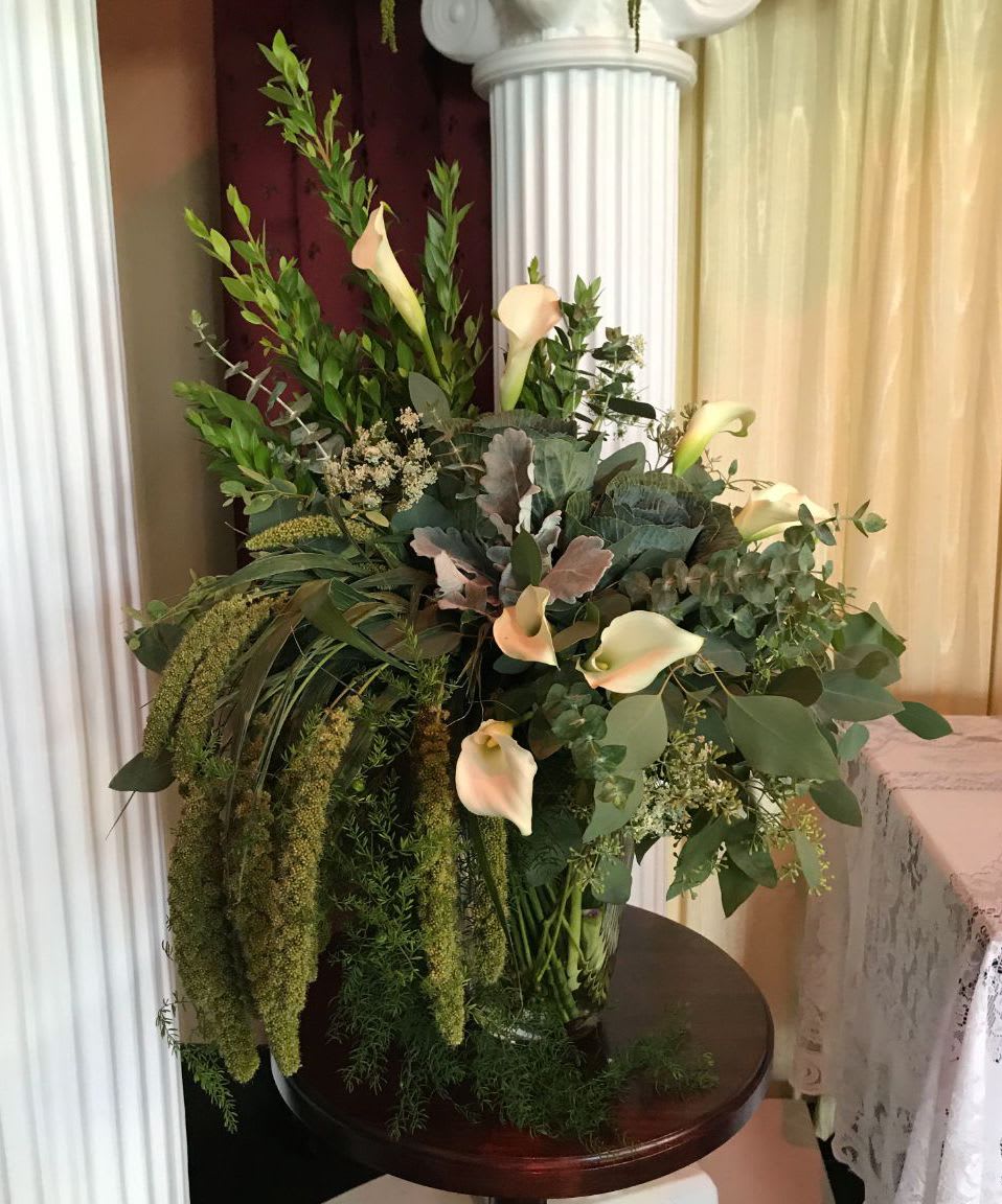 Tall arrangement of cream calla lilies and abundant cascading greenery in a clear glass vase