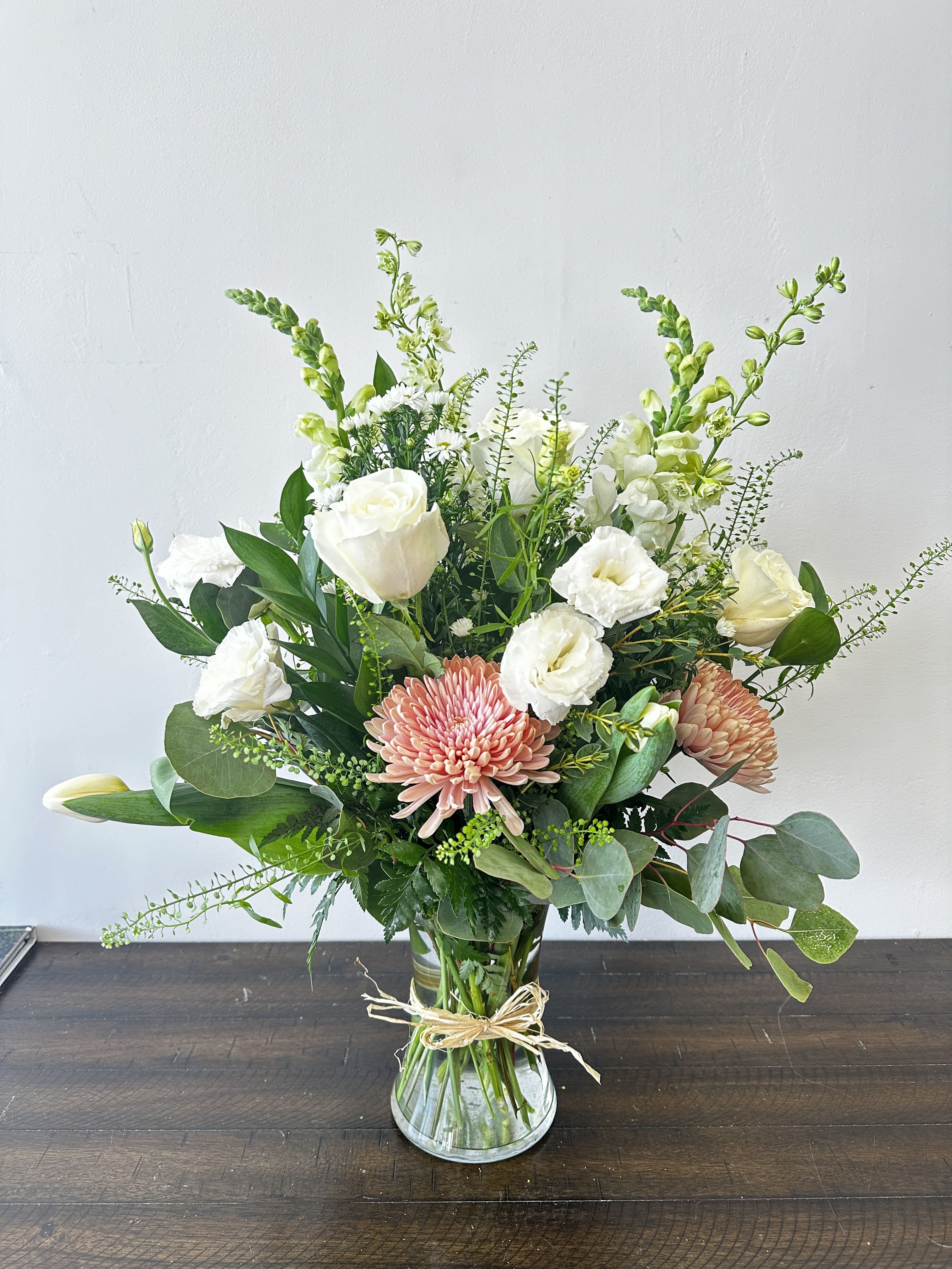 Mixed arrangement of white roses, snapdragons, and peach chrysanthemums in a clear glass vase