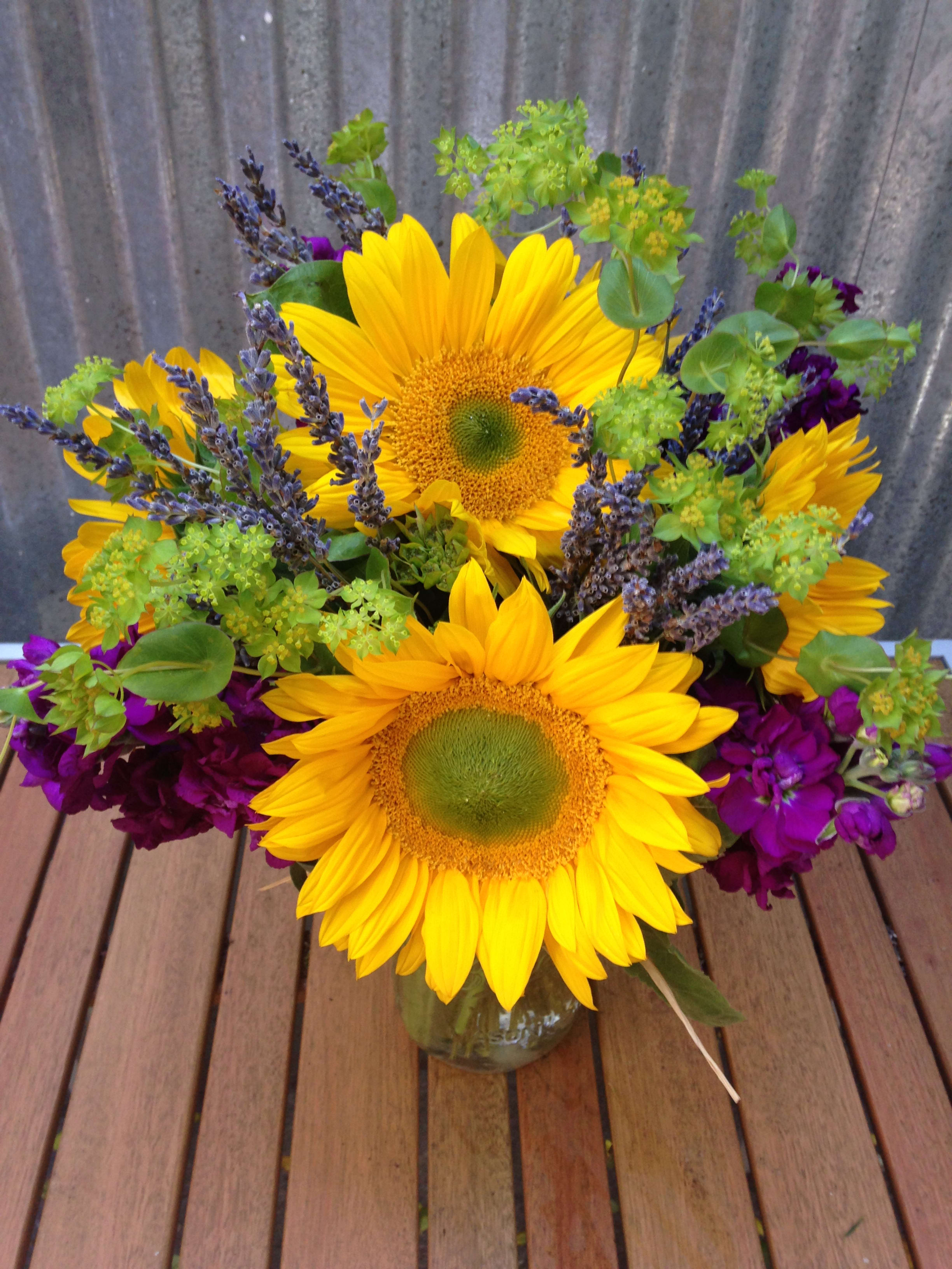 Bright sunflower arrangement with purple flowers in a clear glass vase on a wooden table