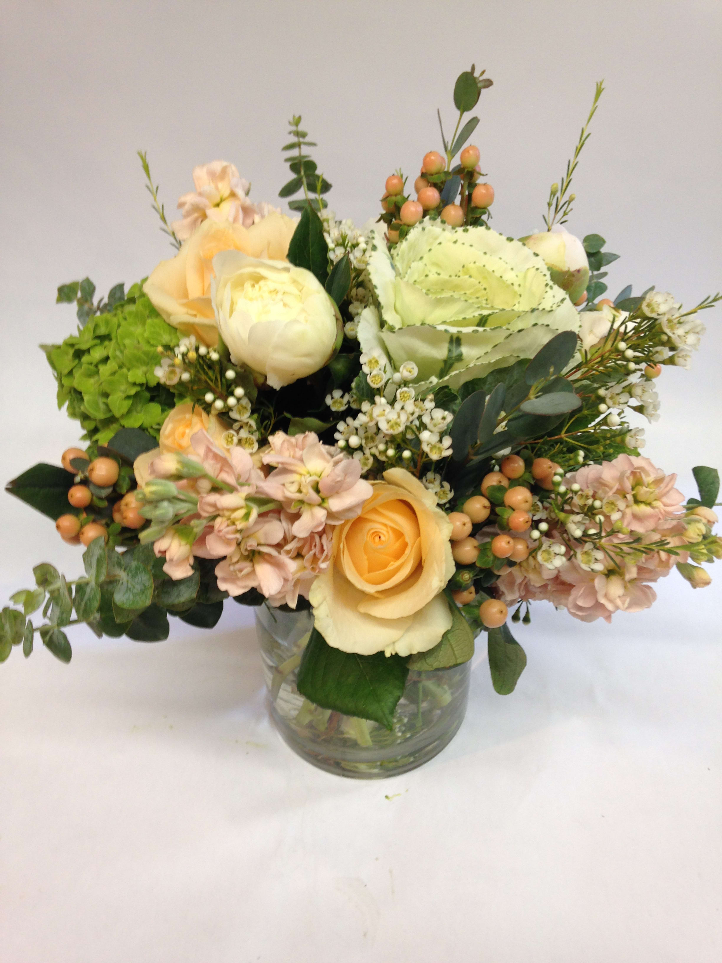 Low arrangement of peach and cream roses with mixed blooms in a clear glass vase