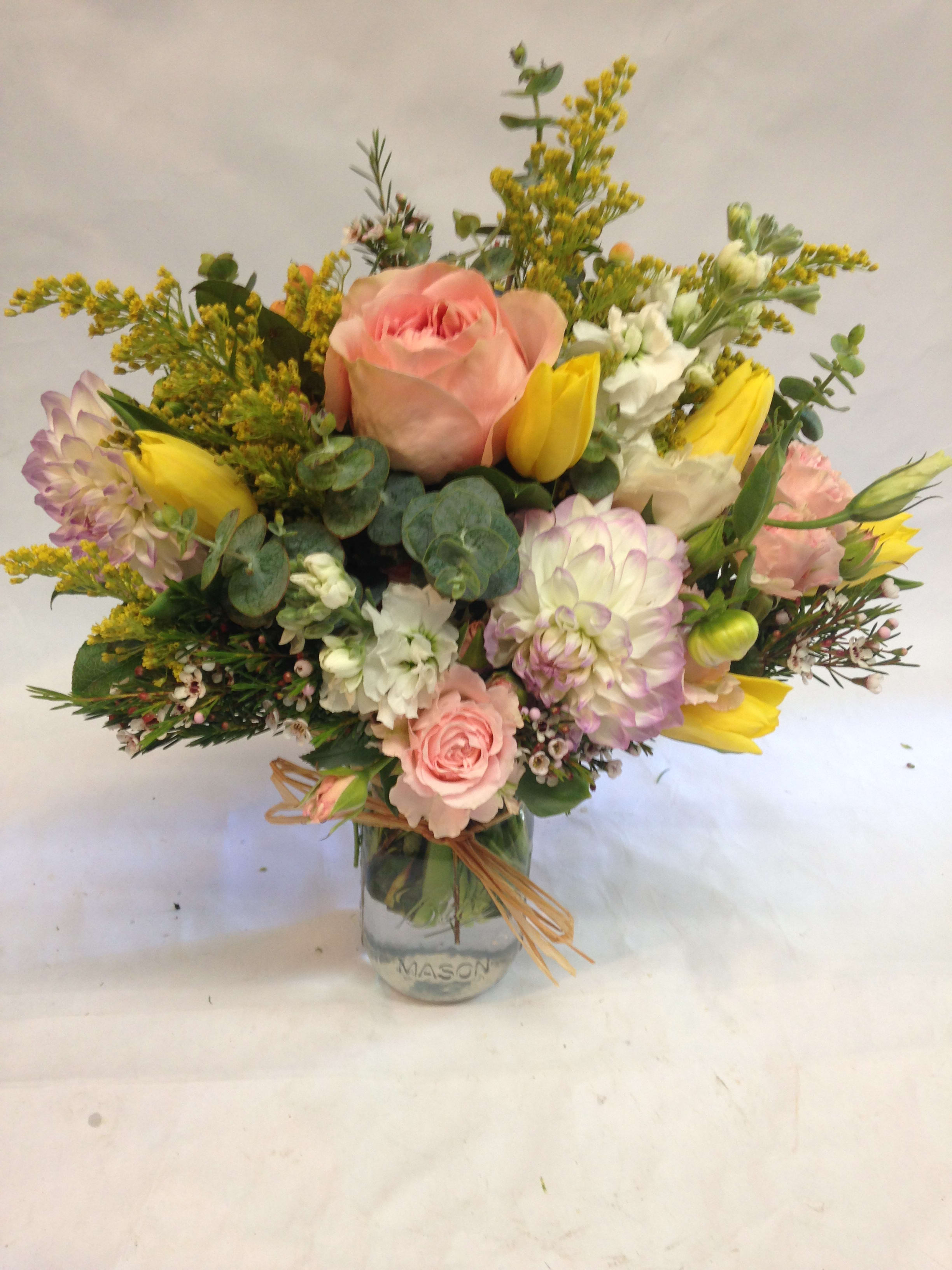 Pastel bouquet of pink roses, yellow tulips, and white blooms arranged in a mason jar vase.