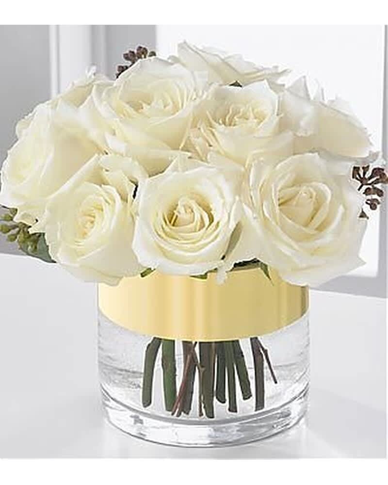 Short arrangement of ivory roses in a clear glass cylinder vase with a wide gold band