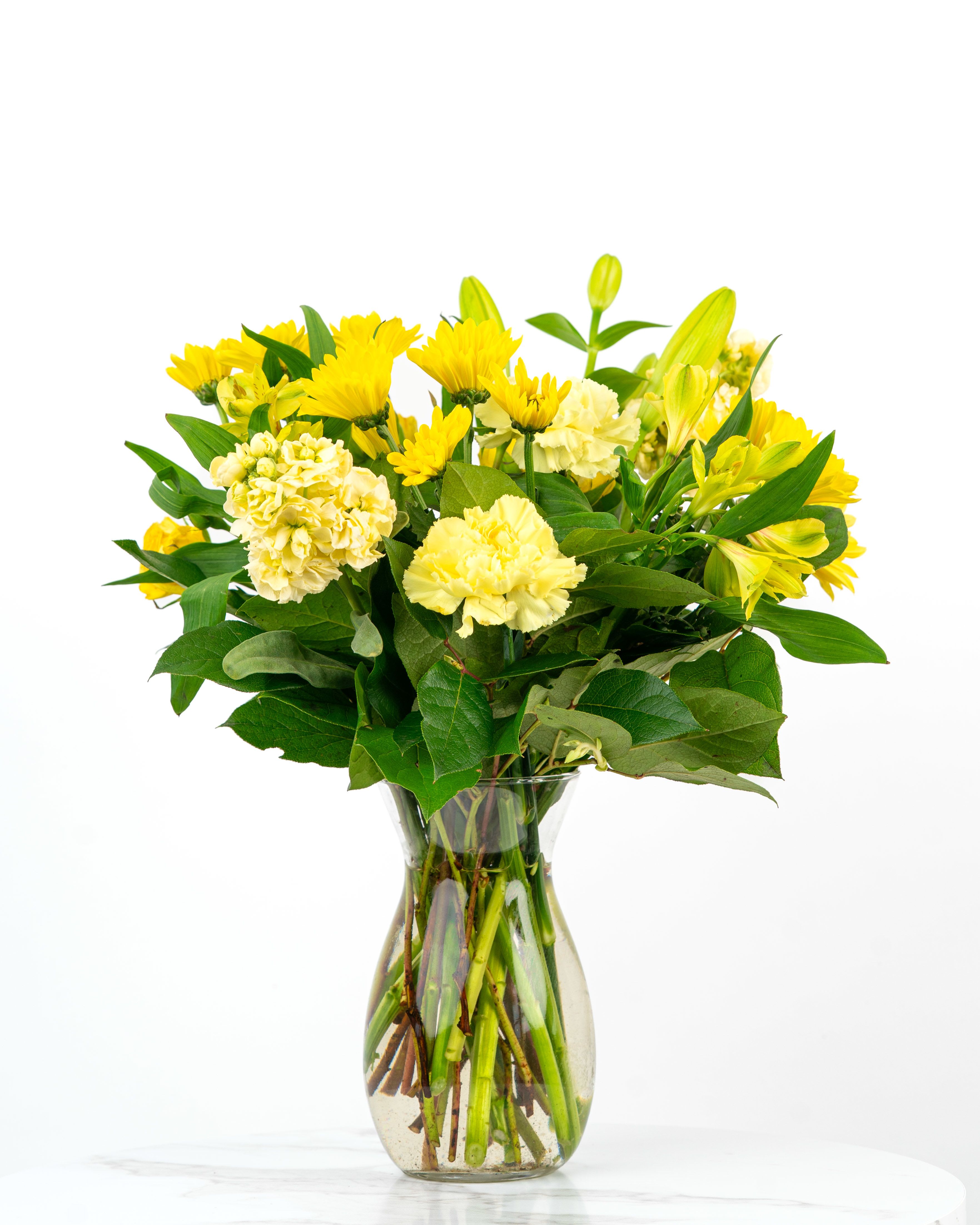 Yellow carnations, chrysanthemums, and lilies arranged in a clear glass vase