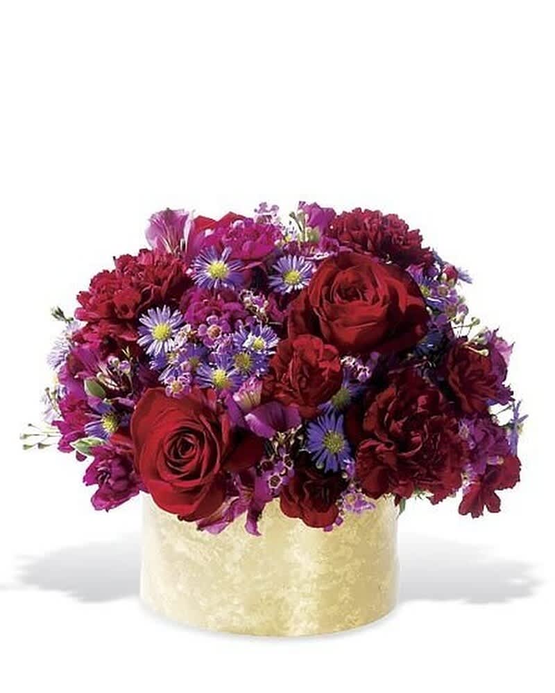 Low arrangement of red roses, red carnations, and purple asters in a cream round box