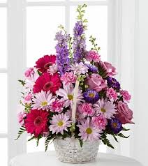 Basket arrangement of pink gerbera daisies, roses, and lavender blooms in a white woven basket