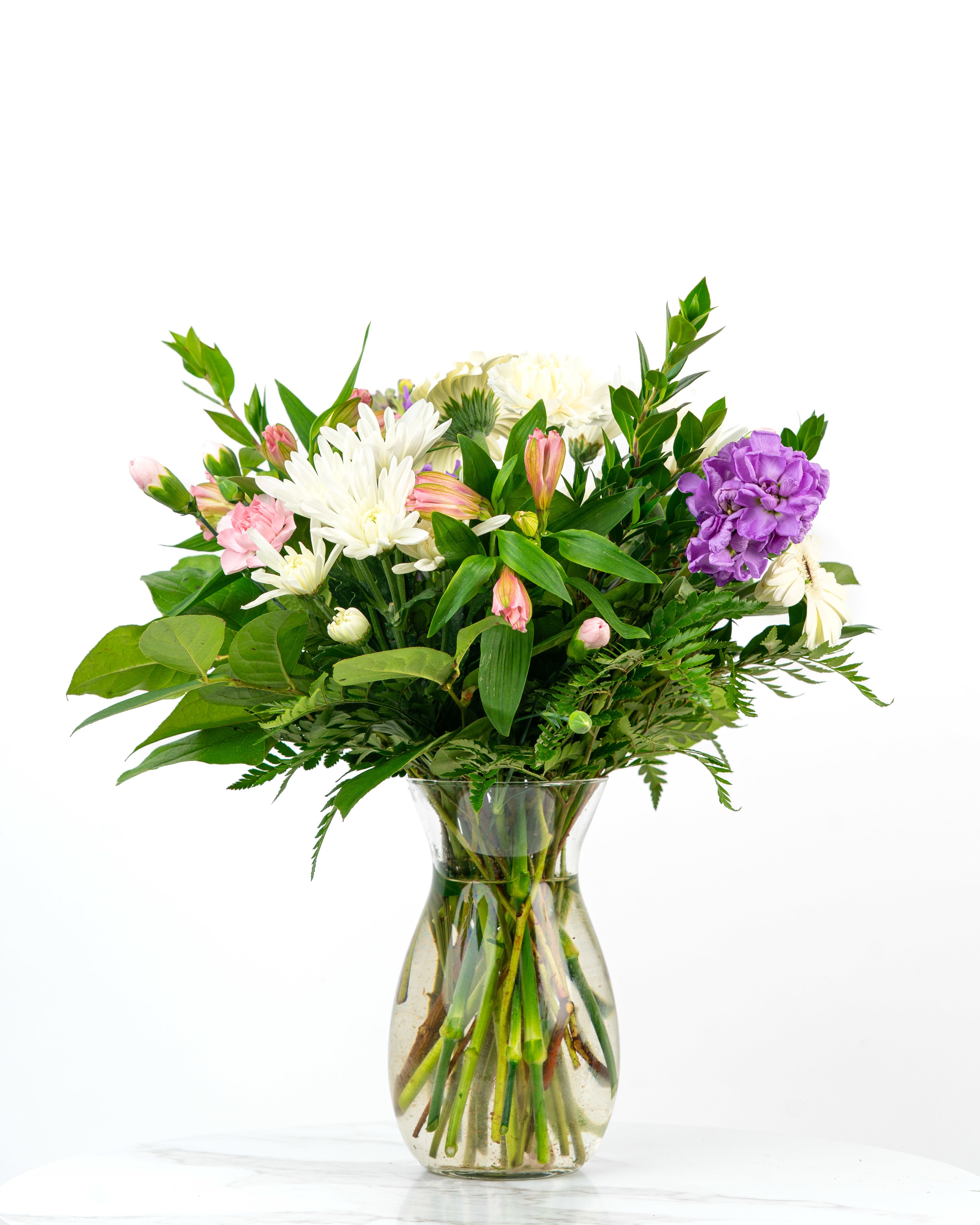 Mixed bouquet of white mums, pink alstroemeria, and a purple carnation in a clear glass vase